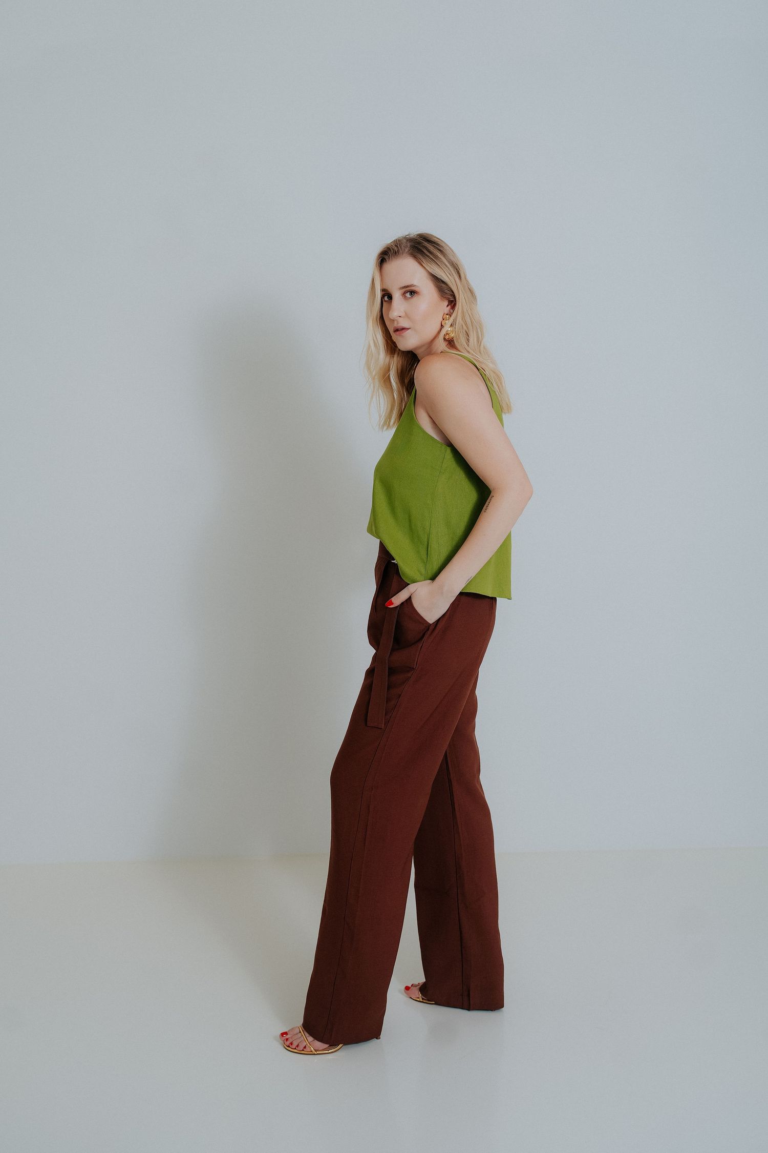 Model wearing a green sleeveless top and brown wide-leg pants poses against a white backdrop.