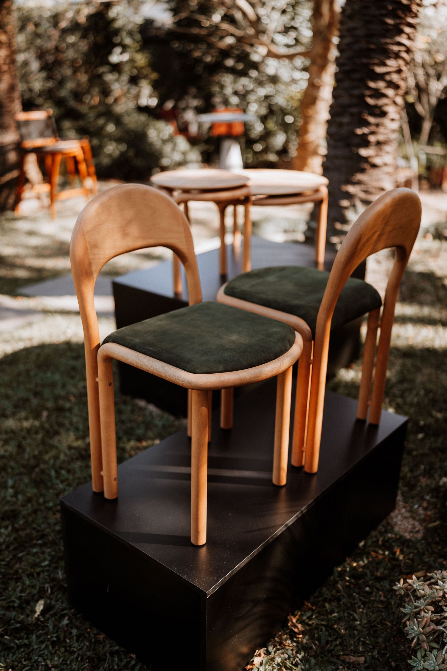 Modern wooden chairs with dark cushions arranged on a sleek black platform in an outdoor setting.