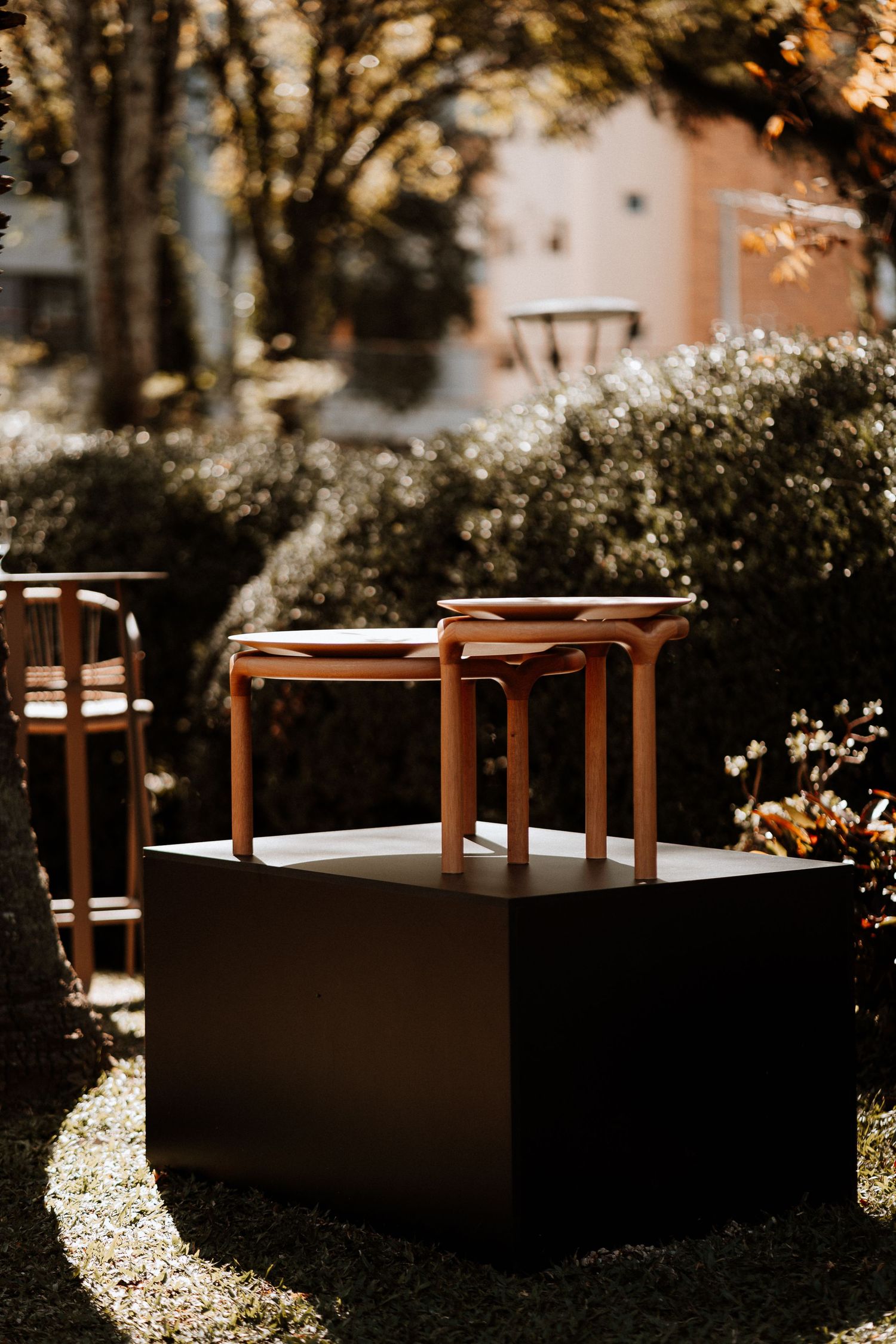 Minimalist outdoor lounge area with wooden furniture and concrete elements in dappled sunlight.