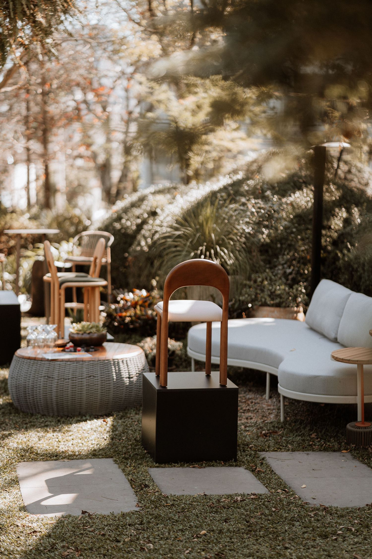 Cozy outdoor seating area with rattan furniture and white cushions arranged under dappled sunlight in a garden setting.