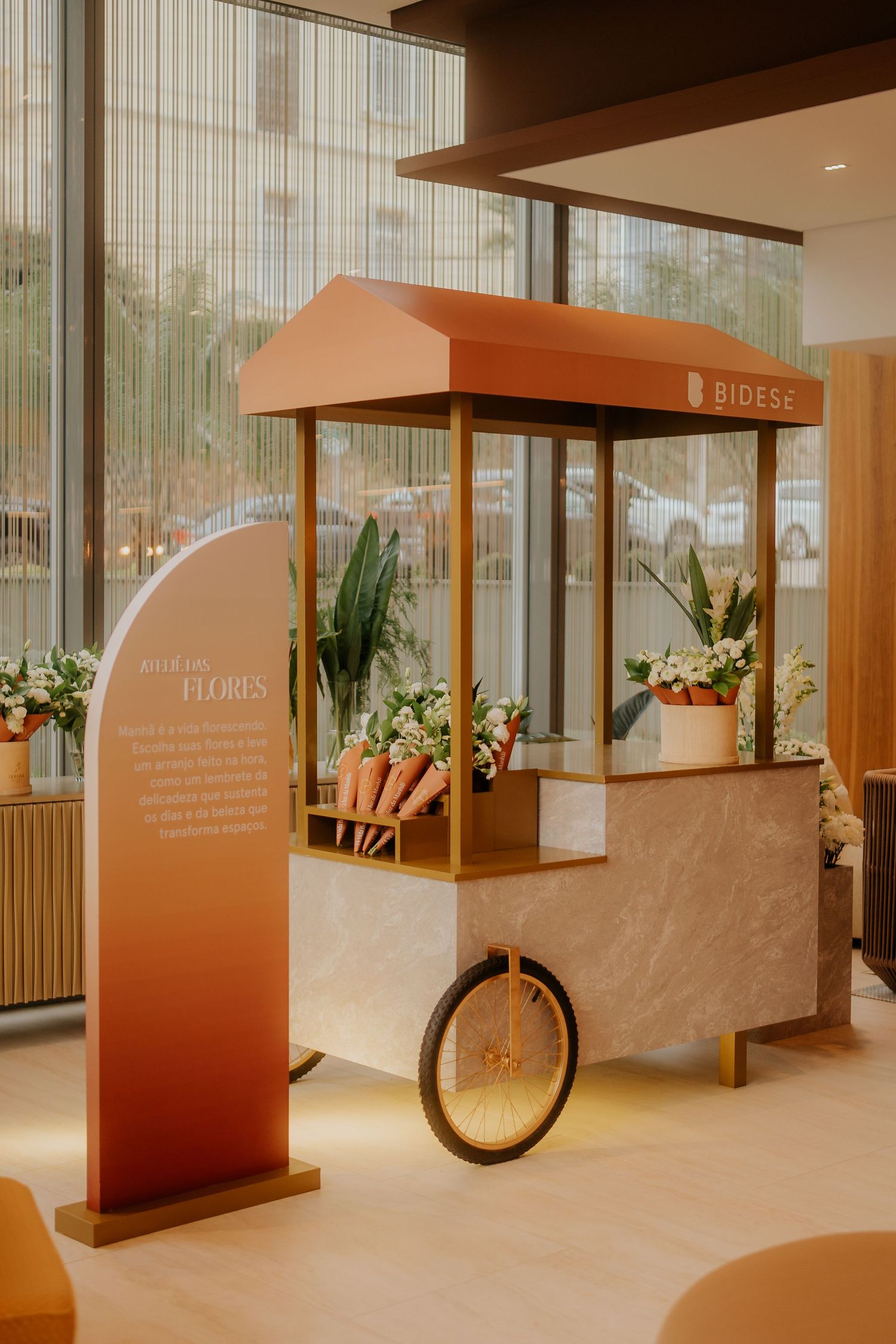 Modern exhibition space with wooden display stands and orange accents featuring floral arrangements and bicycle elements.