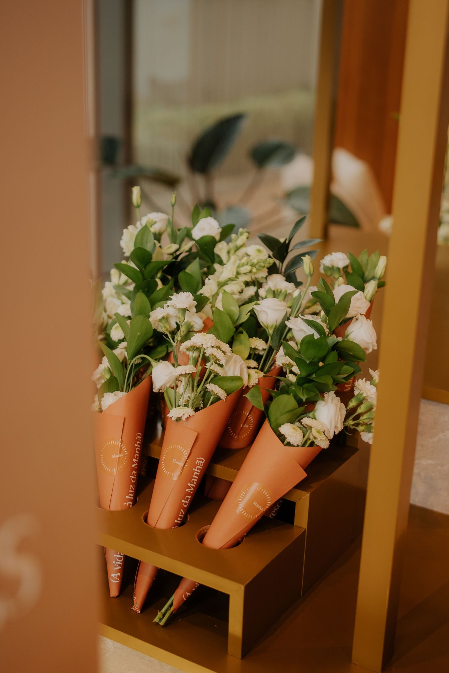 Row of white flowers arranged in orange cone-shaped holders displayed on wooden shelving.