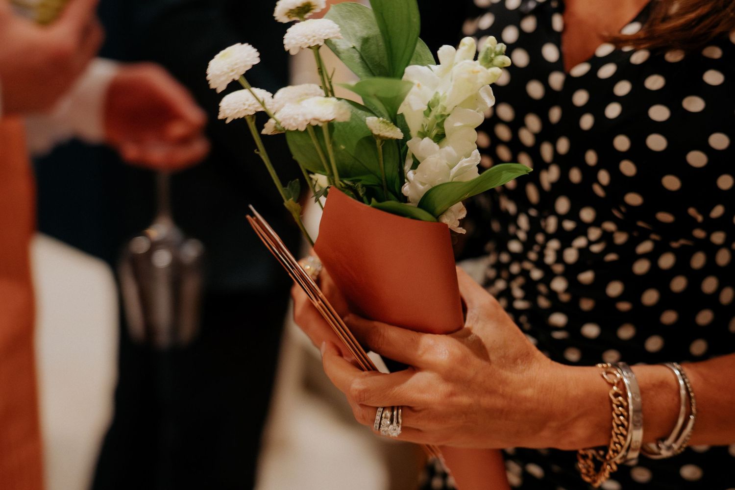 Close-up of hands holding white floral bouquet against black and white polka dot background.