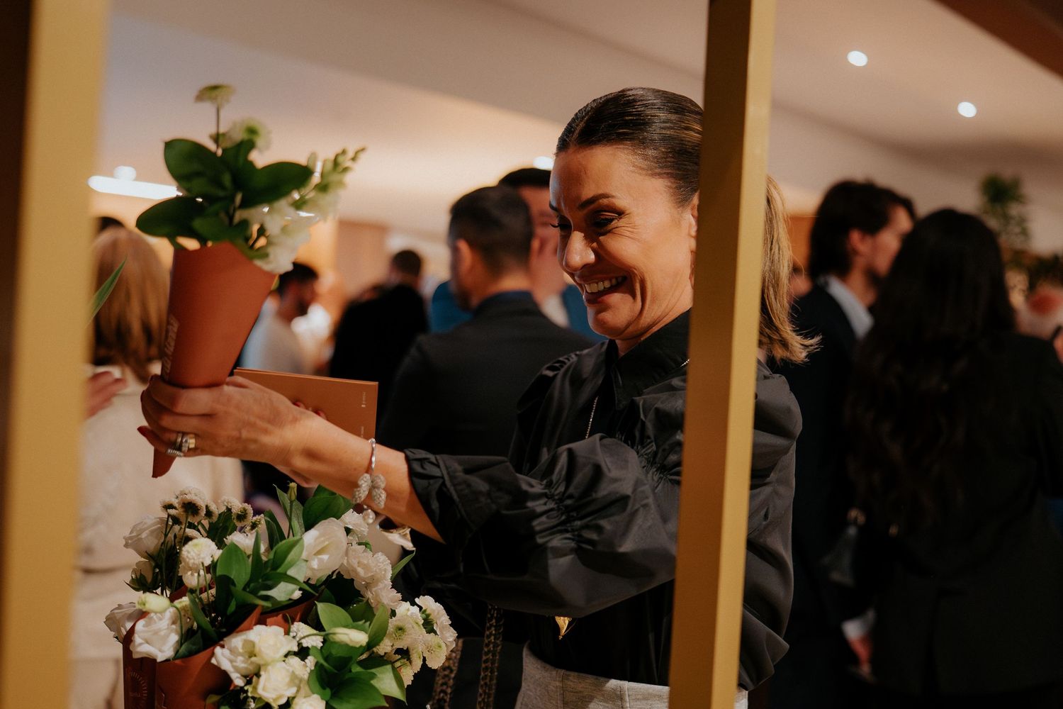 Event staff in black uniforms arrange white floral arrangements in a warmly lit indoor venue.
