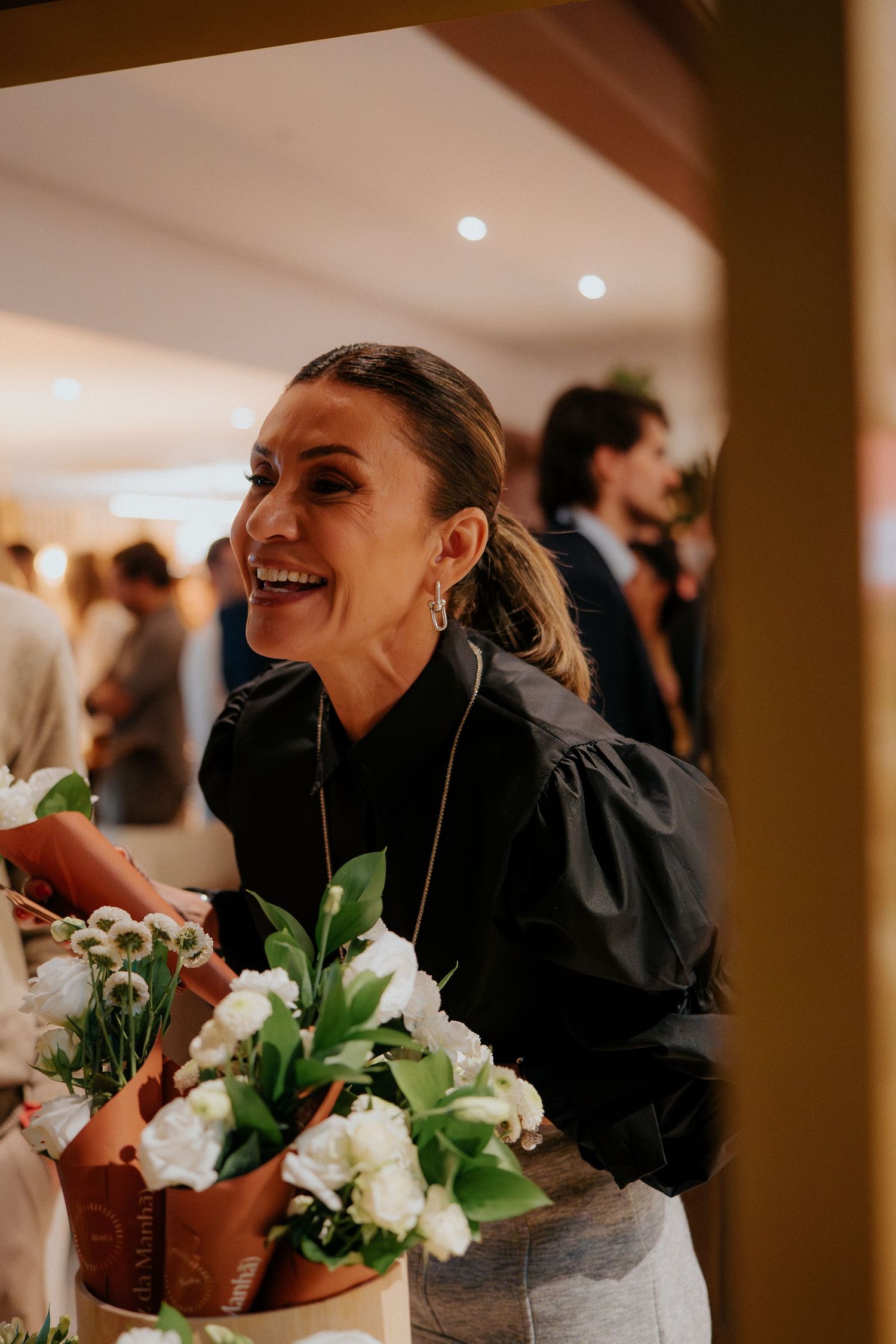 Service workers in dark attire prepare floral displays at an elegant indoor event.