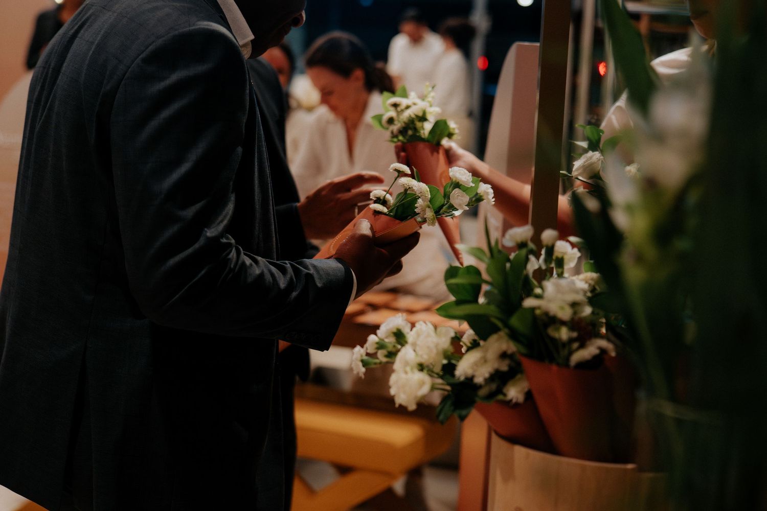 Close-up of hands arranging delicate white floral arrangements in terracotta pots during an event setup.
