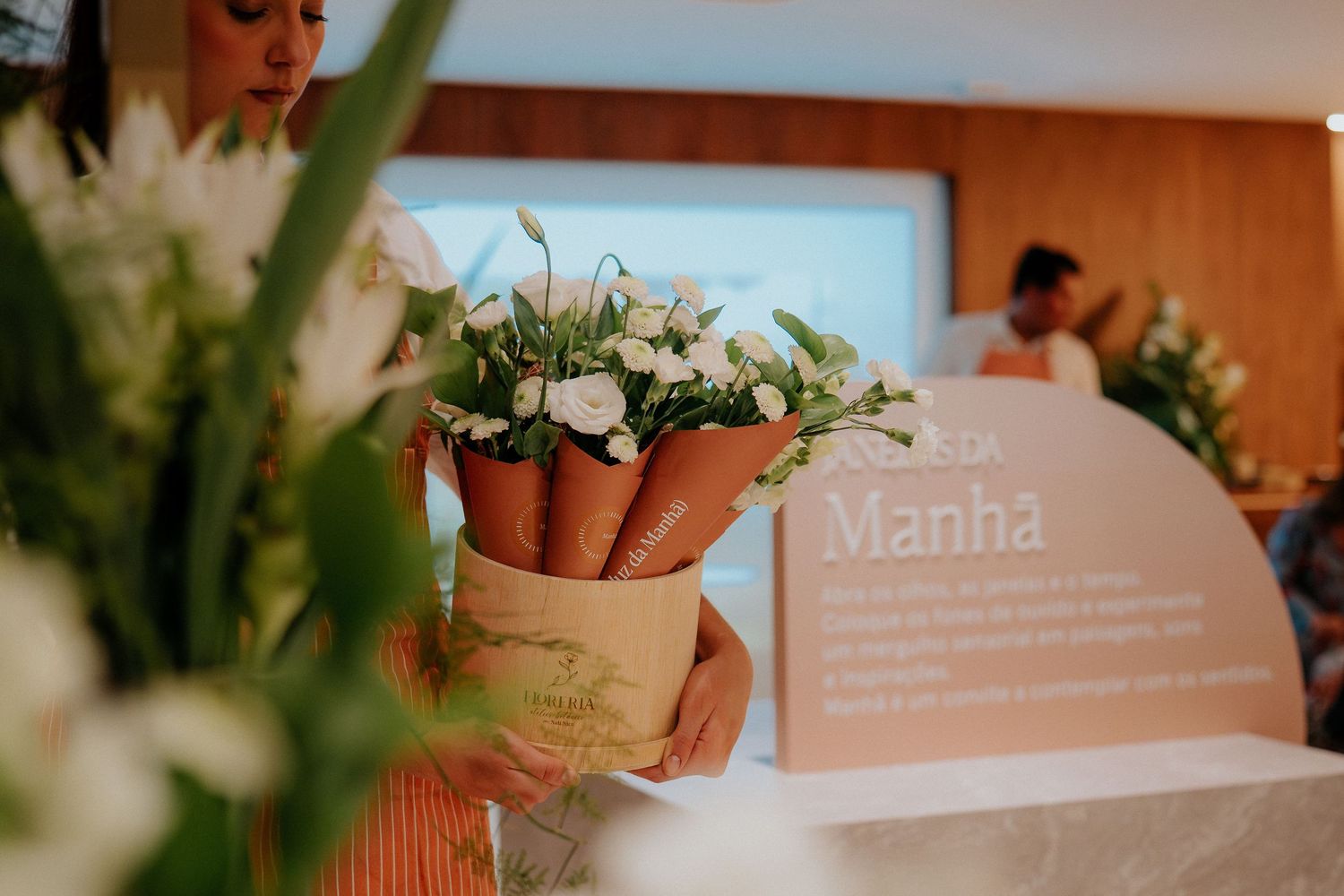 White floral arrangements in terracotta pots displayed near a wooden wall with signage at an event.