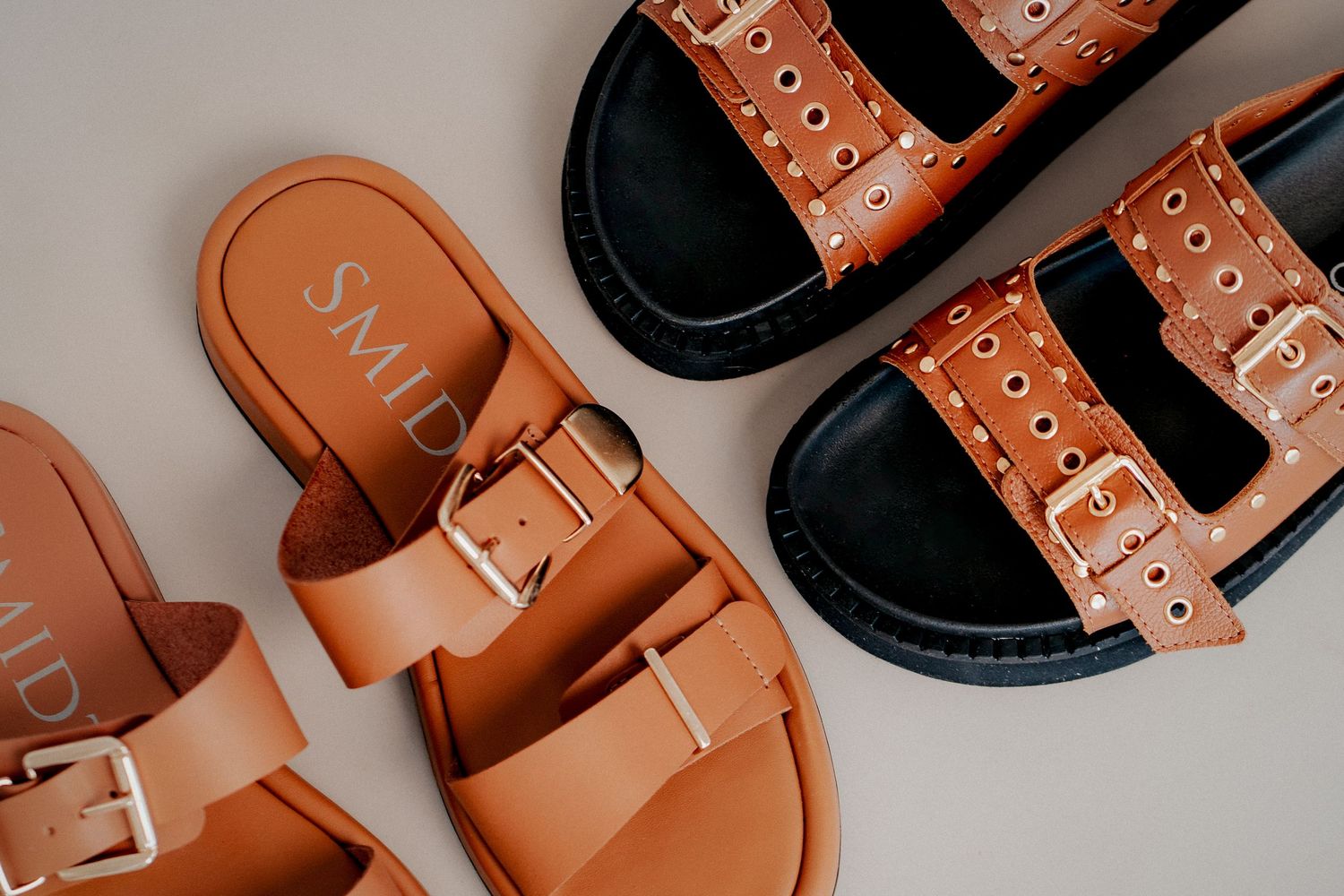 Brown leather sandals with silver buckles and studs arranged in a repeating pattern against a light background.