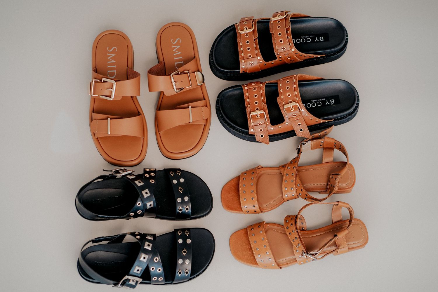 A collection of brown leather and black studded sandals arranged in a row against a light gray background.
