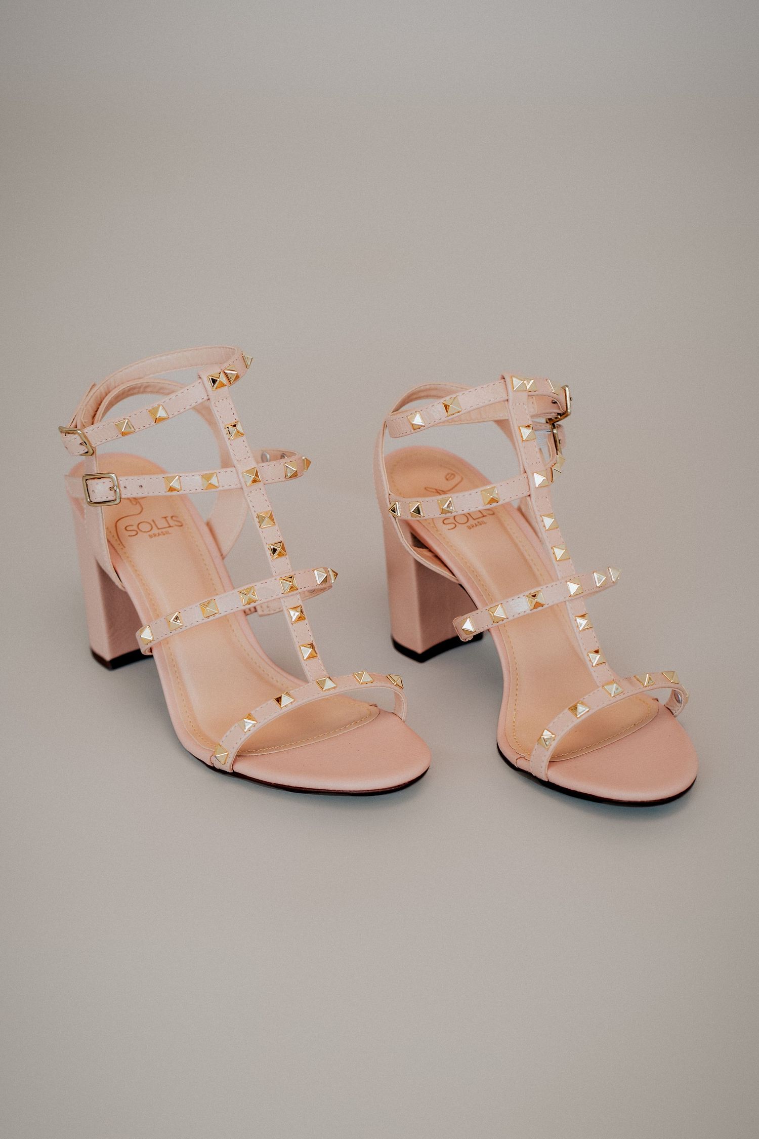 Pale pink studded sandals with block heels shown from multiple angles on a light gray background.