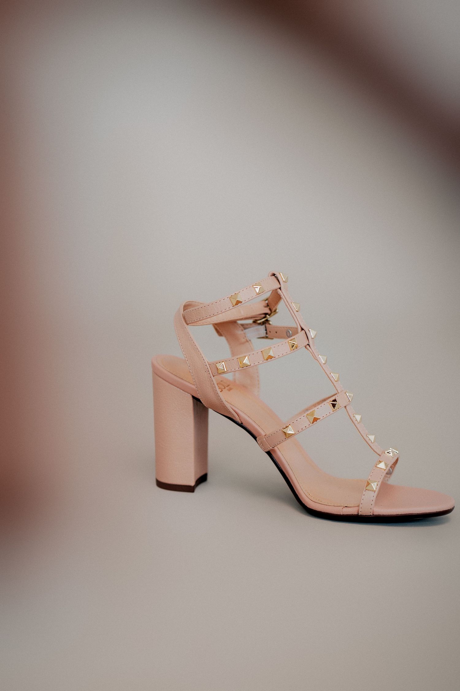 Nude pink studded block heel sandal with T-strap design and metallic accents photographed against light background.