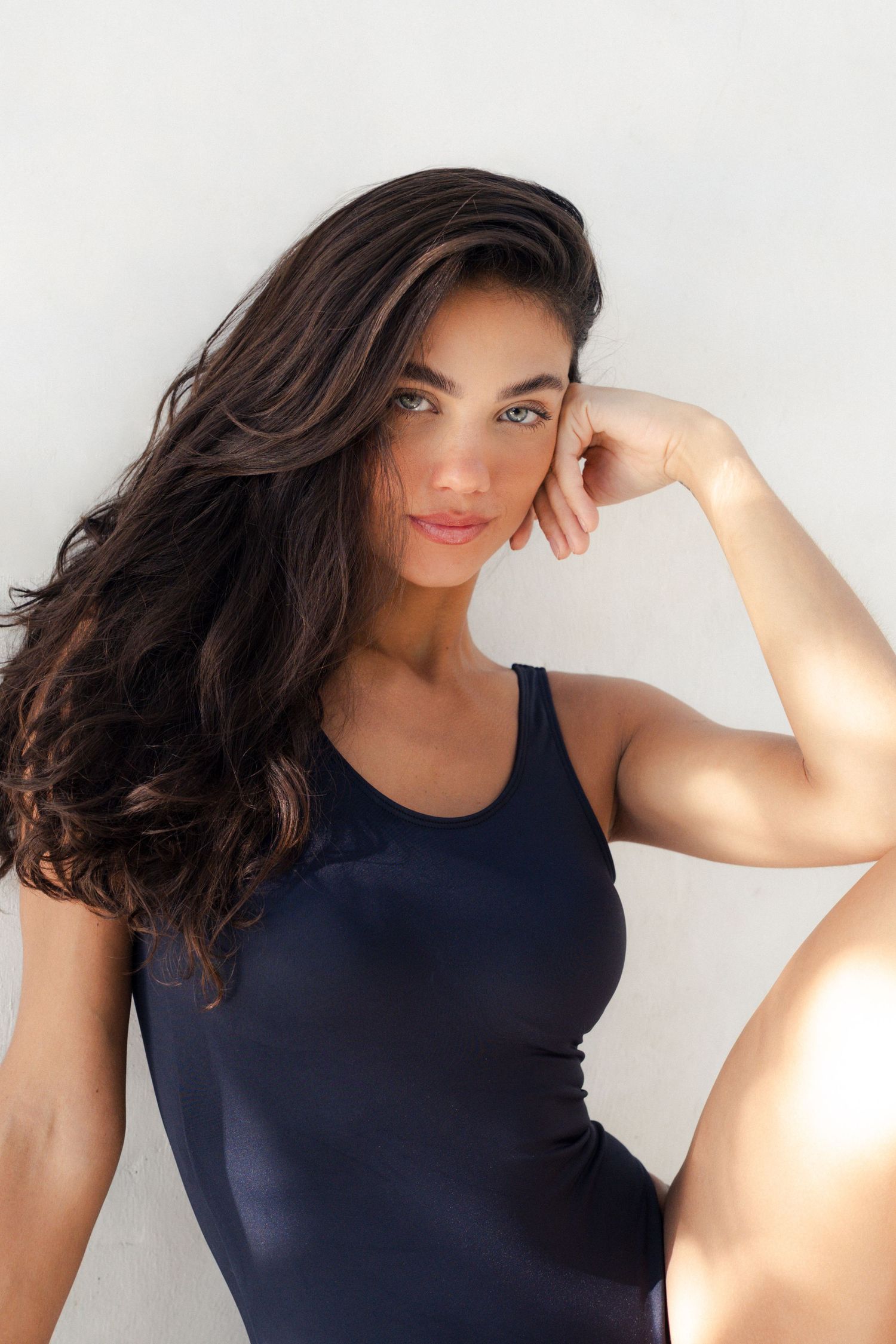 Woman in navy swimsuit posing against white background with natural light.