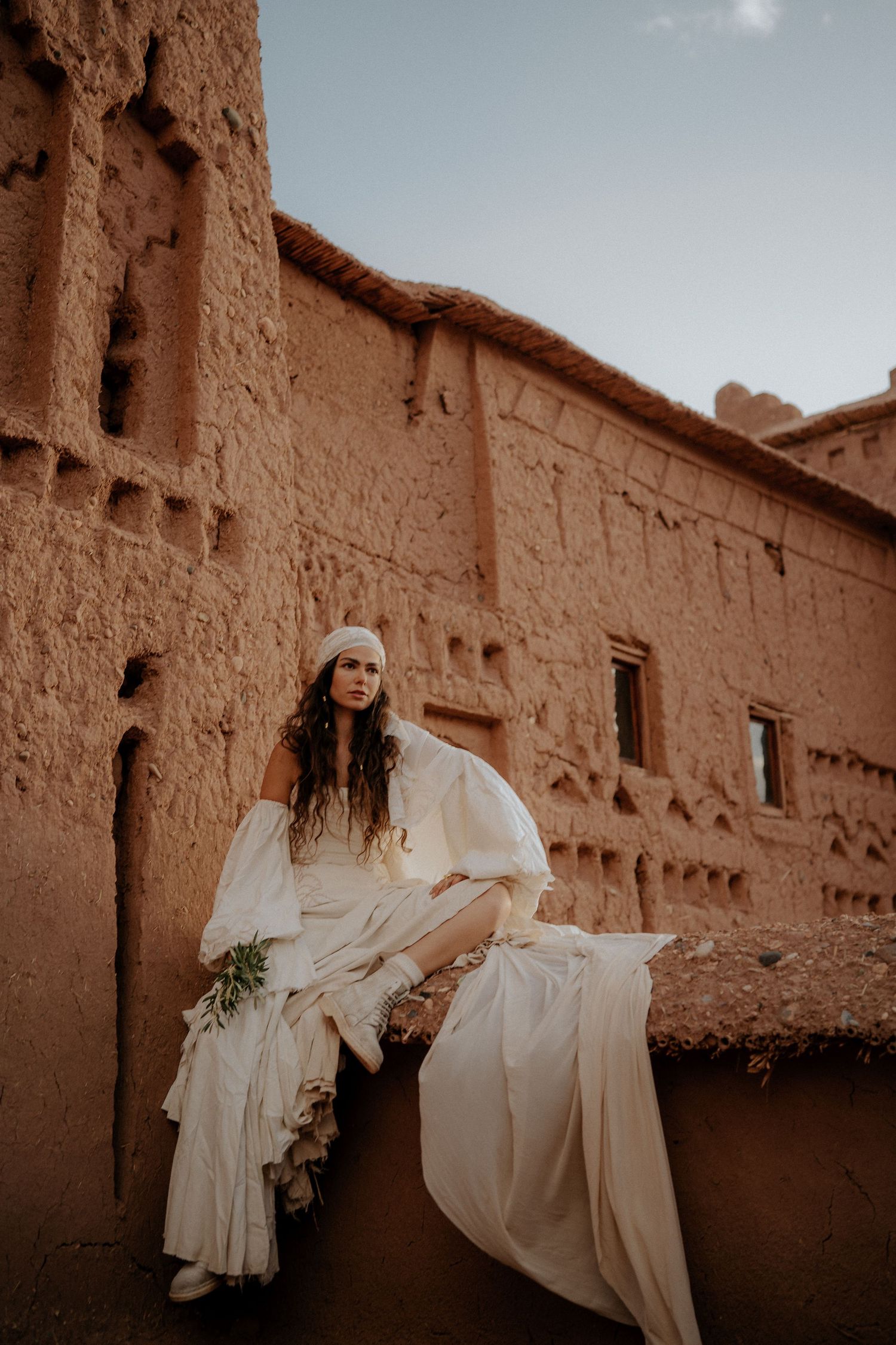 Ethereal figure in flowing white dress moves gracefully against rustic adobe walls in a desert setting.