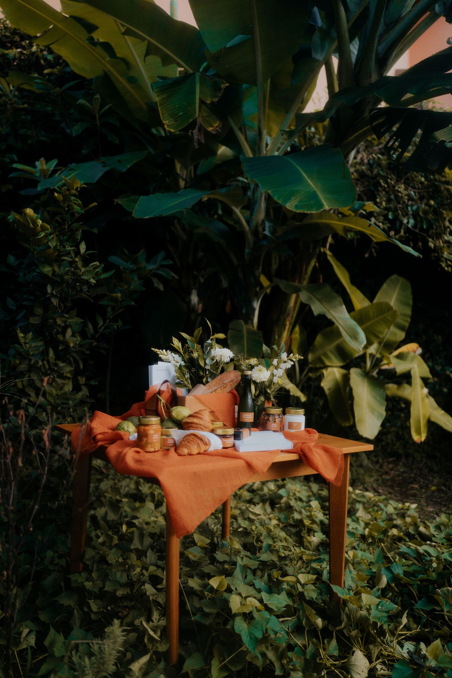A rustic wooden table set against lush green foliage with various items arranged on top.