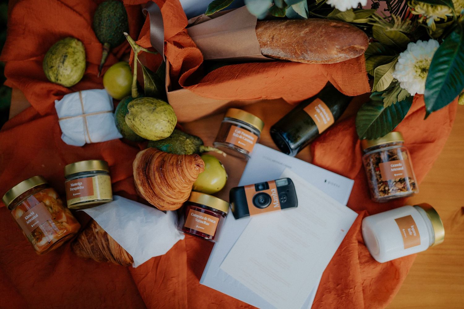 Papers and jars arranged artistically on a terracotta colored surface with greenery in the background.
