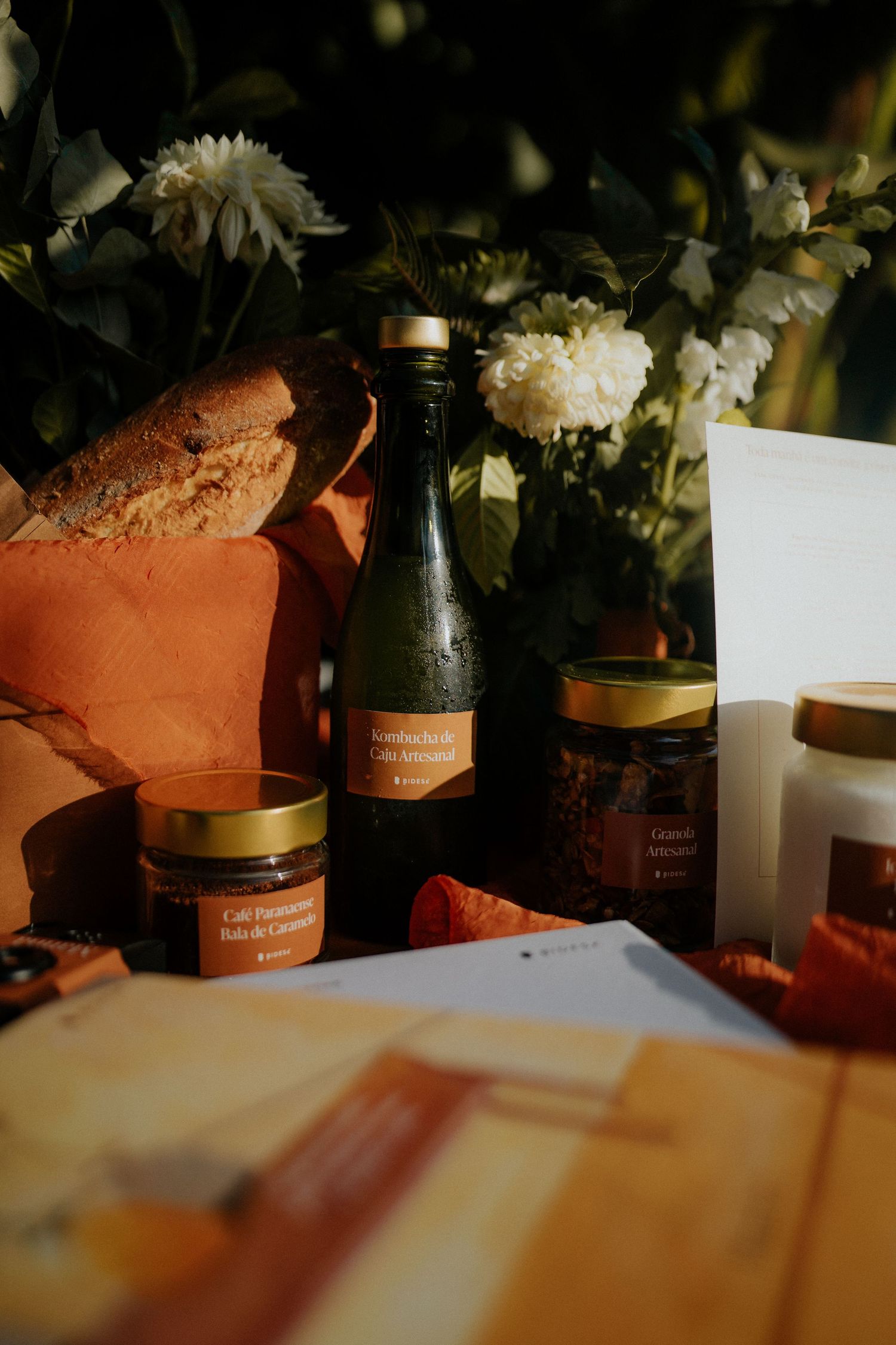 Glass jars and white flowers arranged on a warm-lit surface with papers.