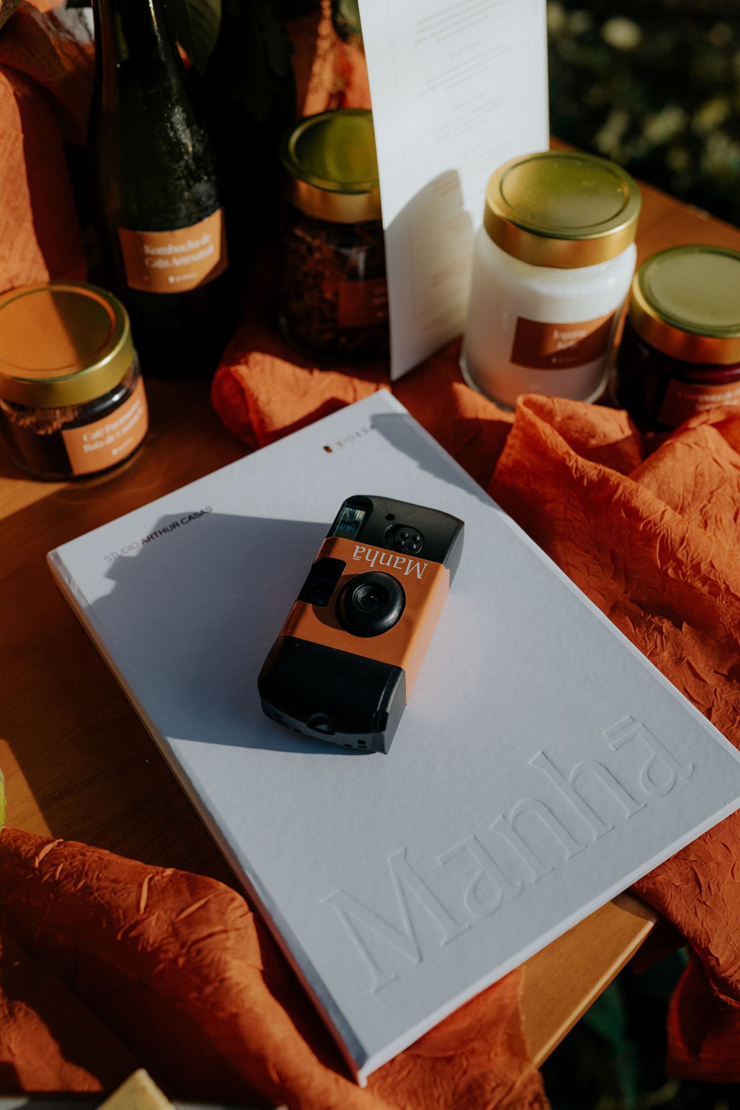 White folder with a vintage camera displayed on orange fabric next to assorted glass jars.