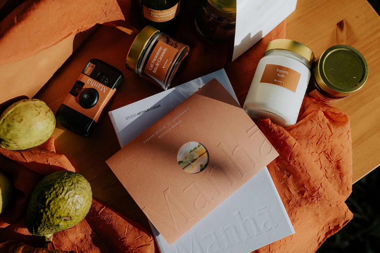 Documents and folders arranged with vintage camera, jars and citrus fruits on orange fabric.
