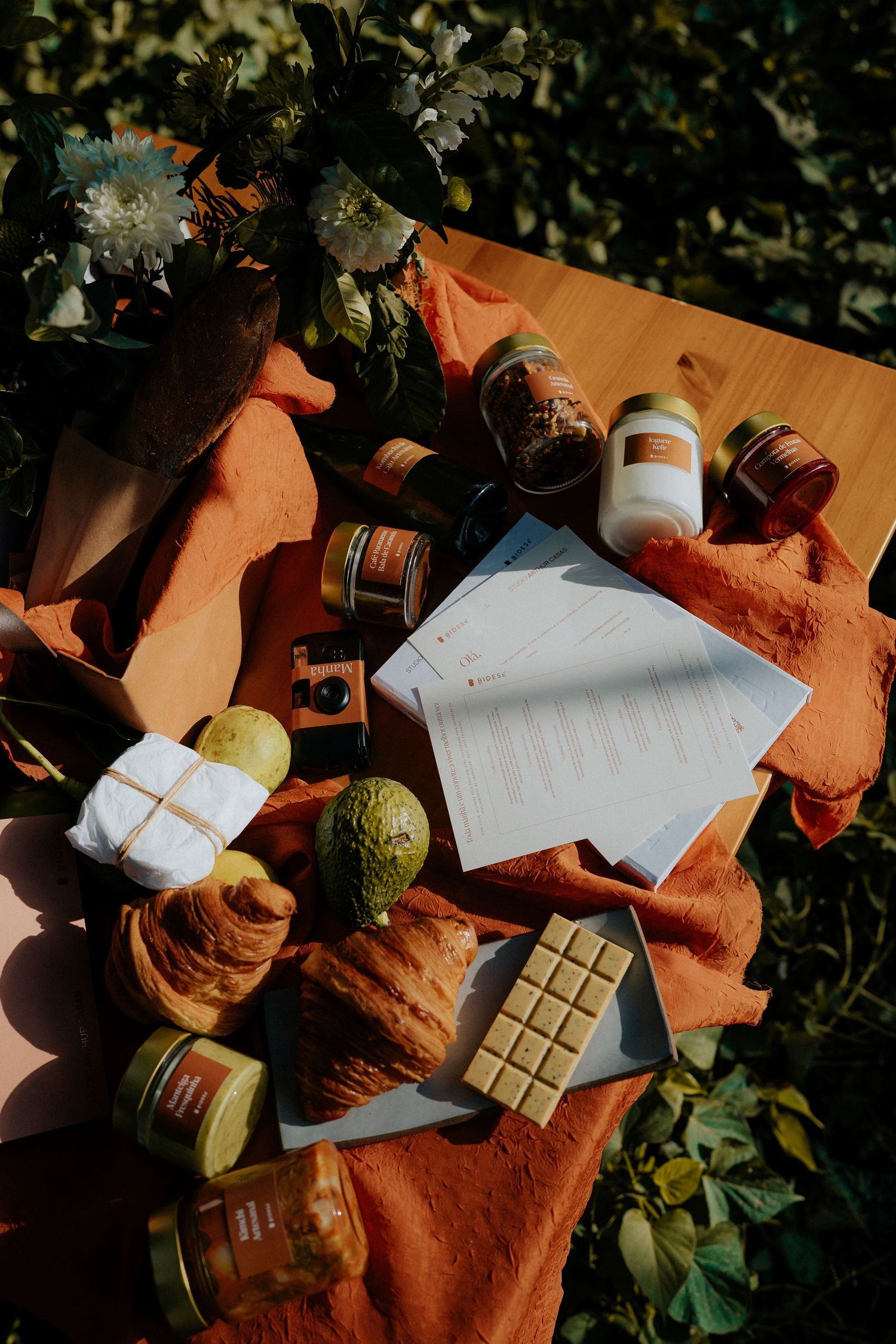 Styled flatlay with croissants, chocolate bars, jars and papers on terracotta colored textile.