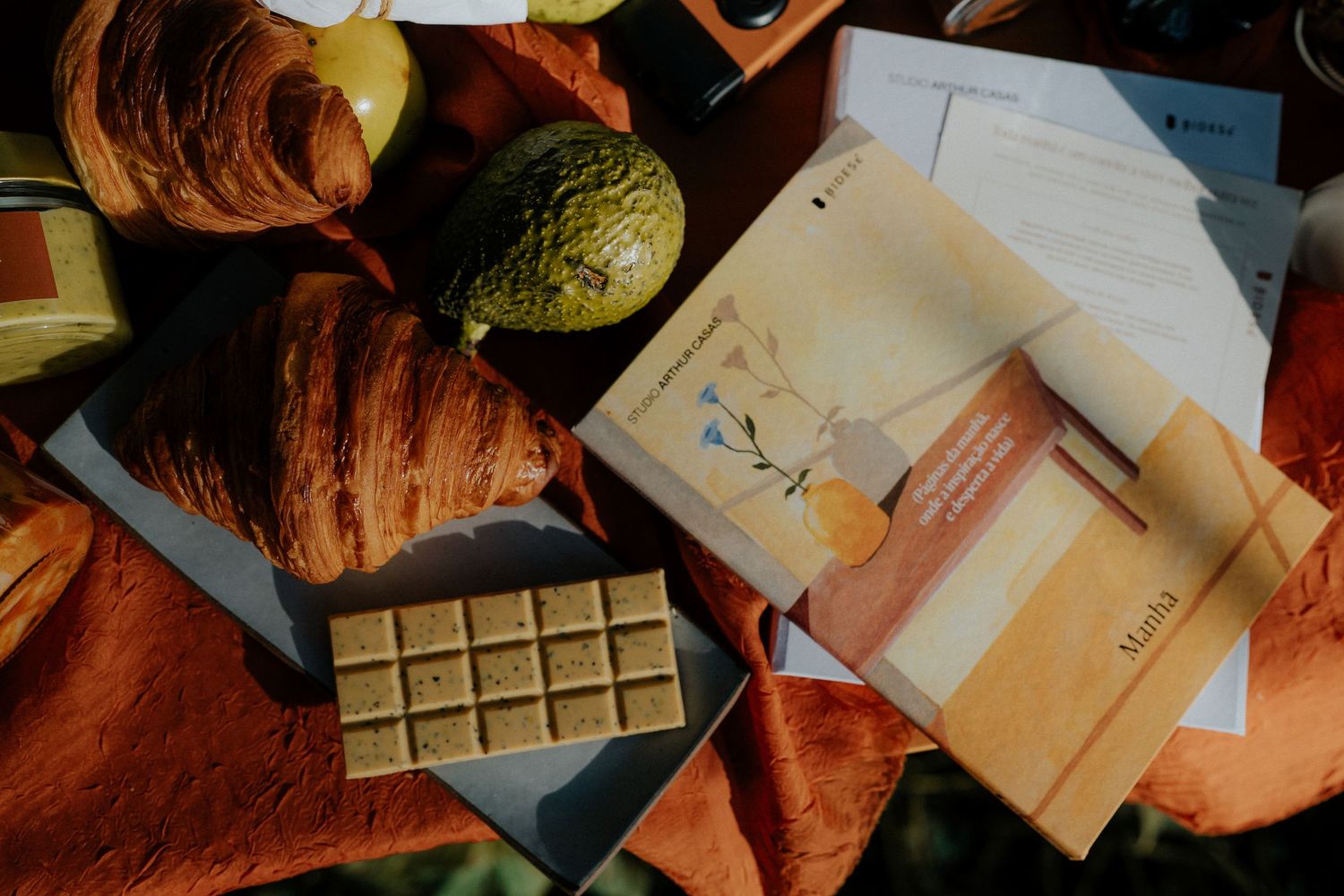Overhead shot of croissants, chocolate bars and documents arranged on orange fabric.