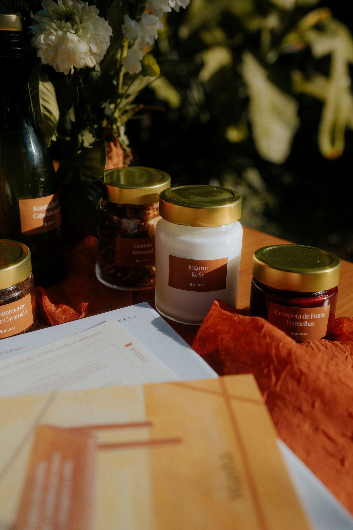 White documents and glass jars arranged on orange fabric with white flowers in background.