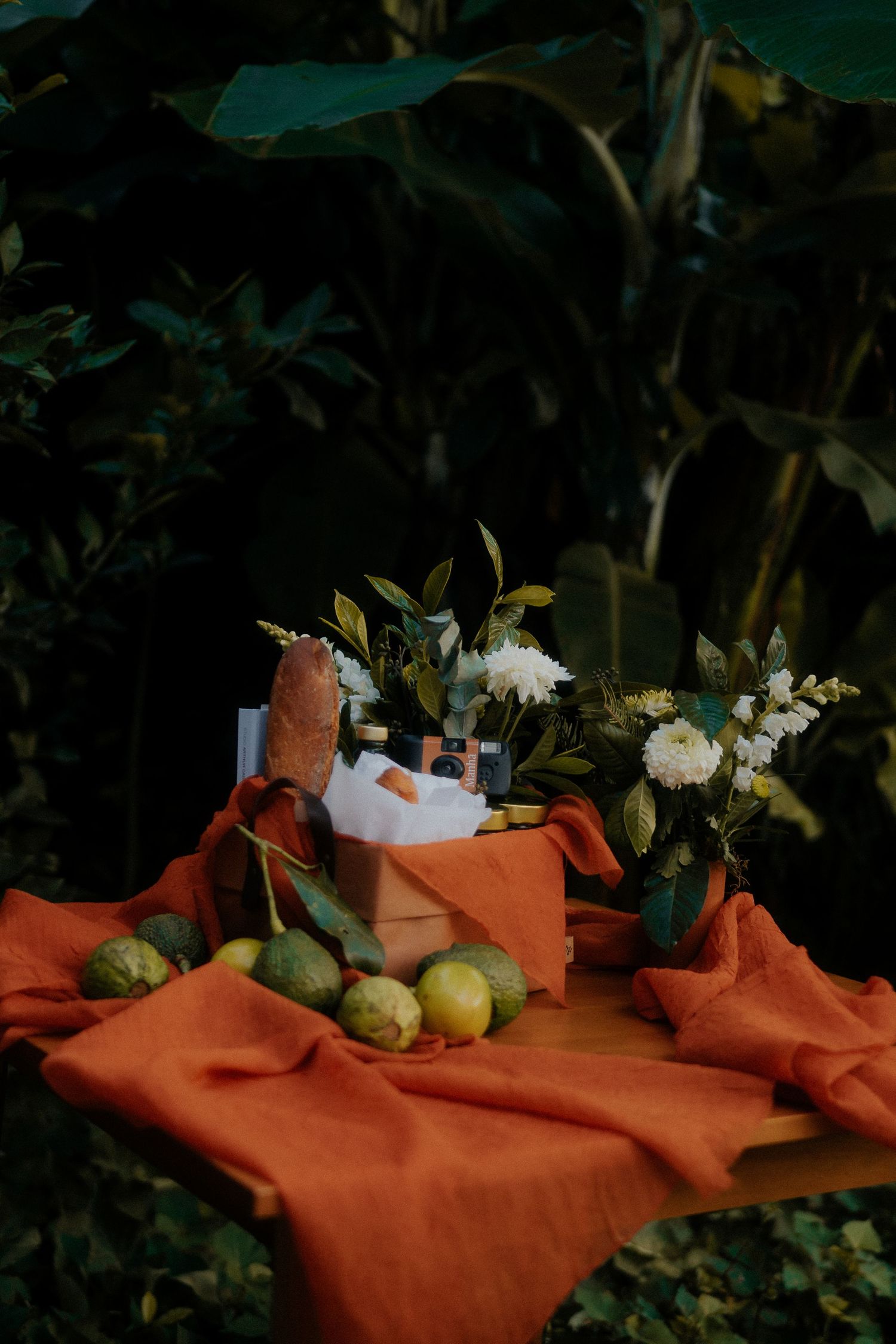 Still life with orange textile, white flowers and citrus fruits in garden setting.