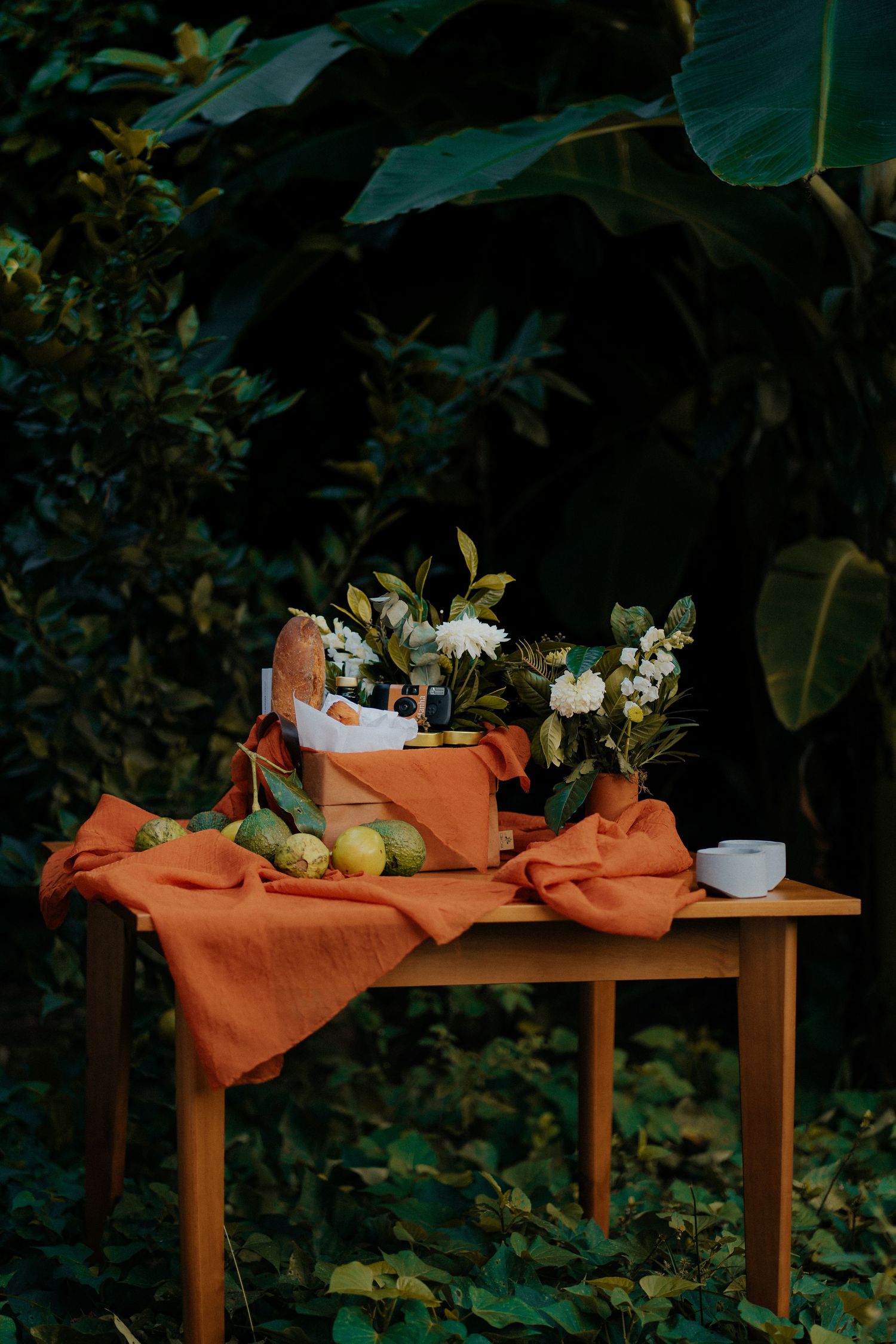Rustic wooden table with orange cloth, flowers and fruits in garden setting.