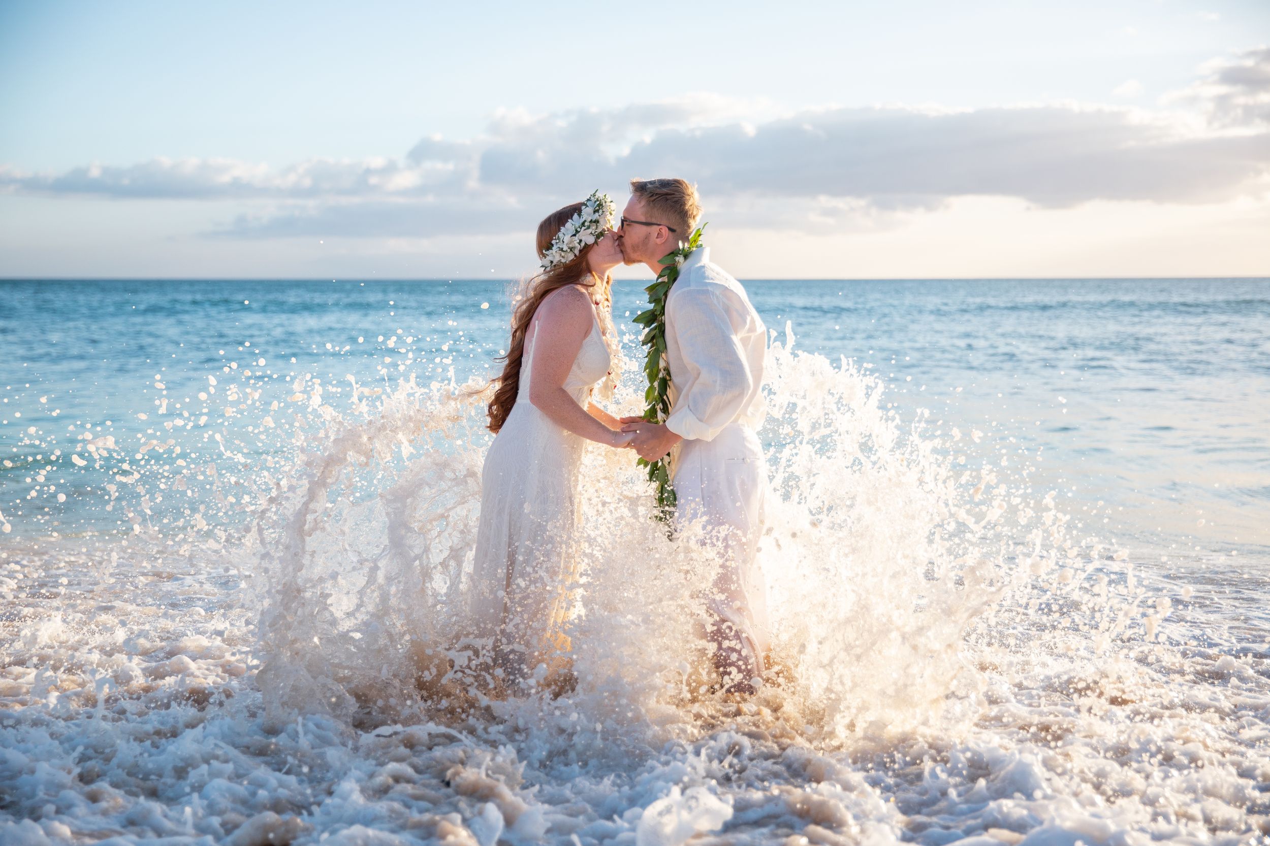 A couple splashes joyfully in the ocean waves at sunset during their romantic wedding in Waikiki.
