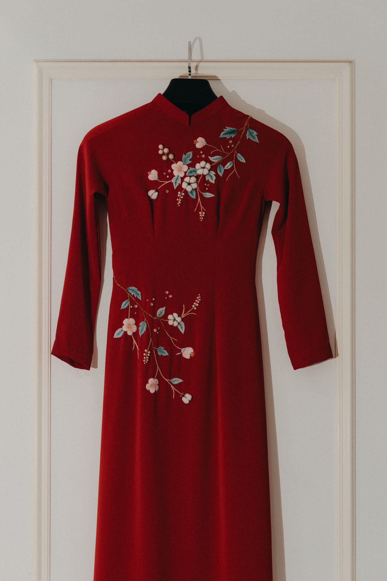 Red Vietnamese ao dai dress with floral embroidery hanging on a door hanger.