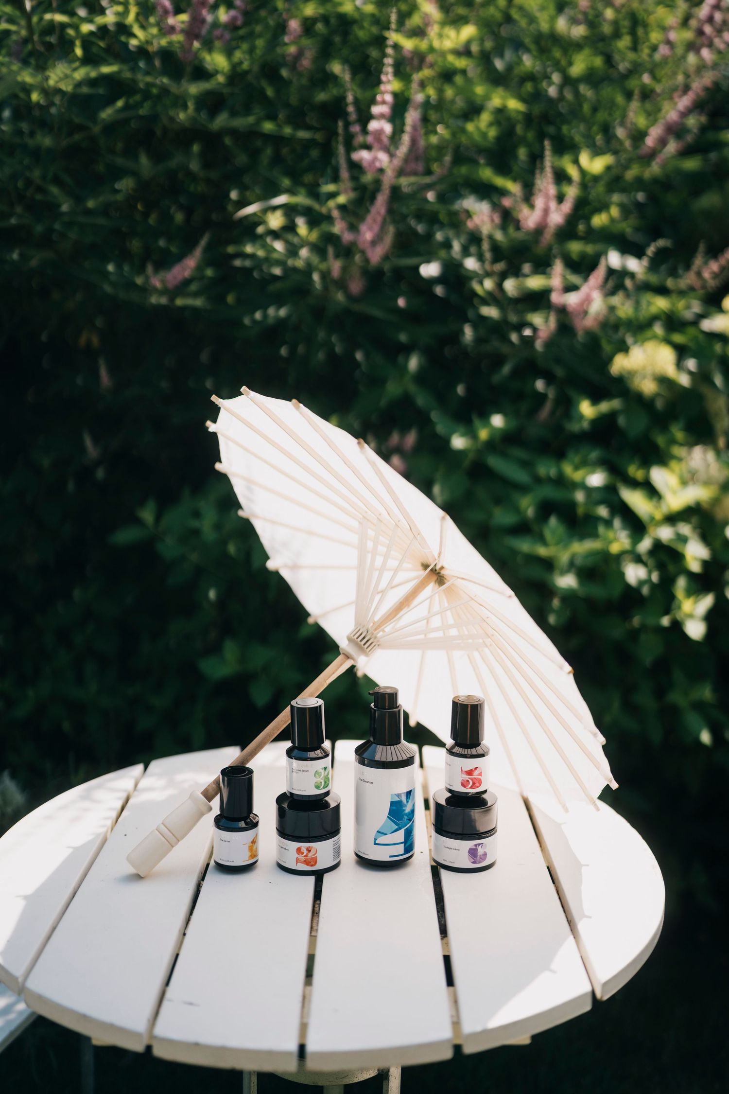 A decorative white paper parasol and assorted bottles displayed on a white wooden table outdoors.