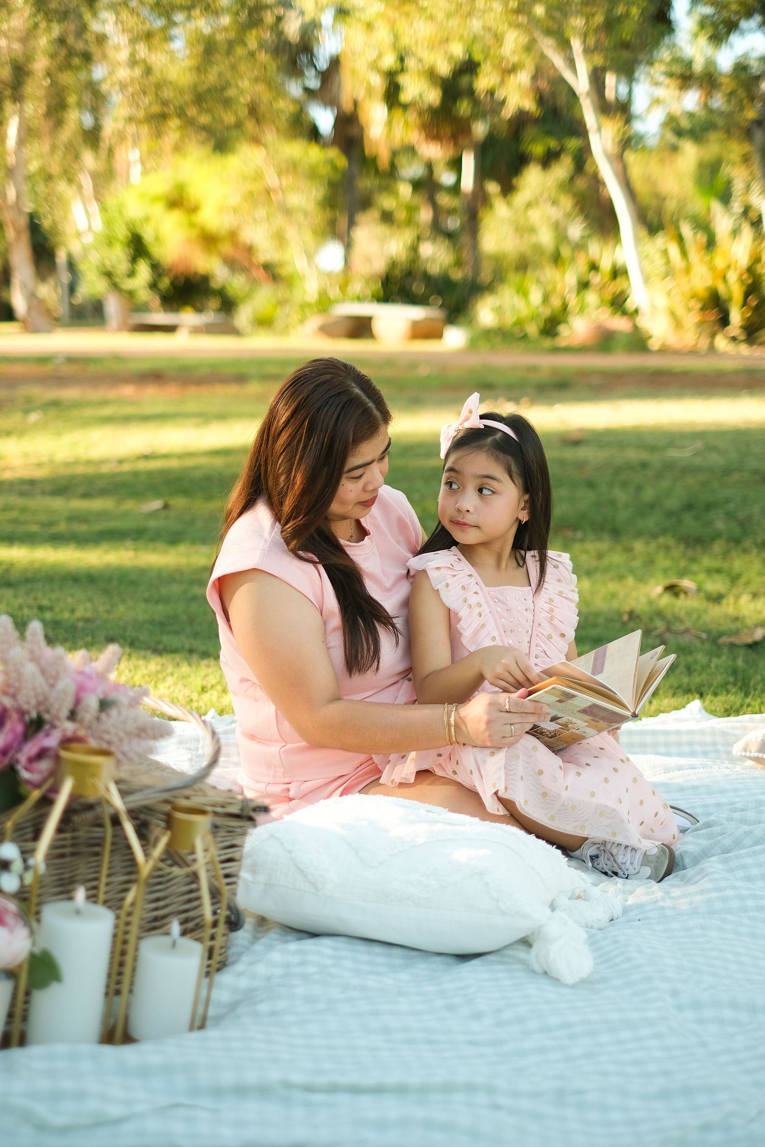 A picnic scene in a sunny park with two people sharing a book on a blanket.