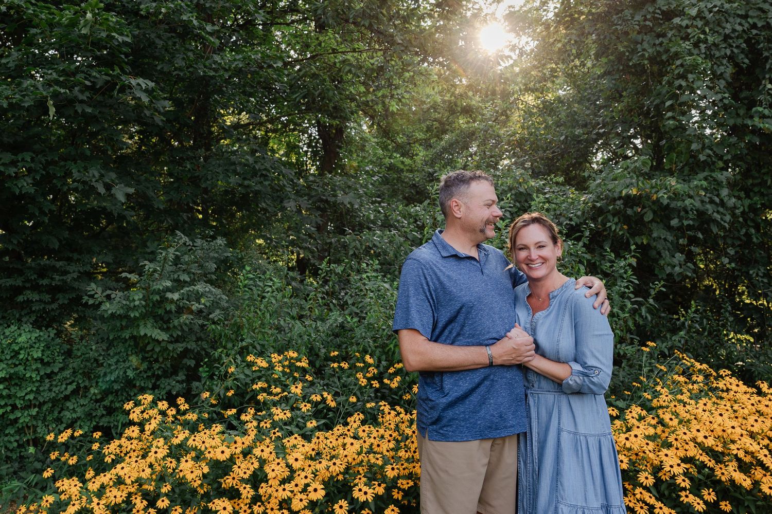 A couple shares a tender moment in front of vibrant yellow black-eyed susan flowers during golden hour in a garden setting.