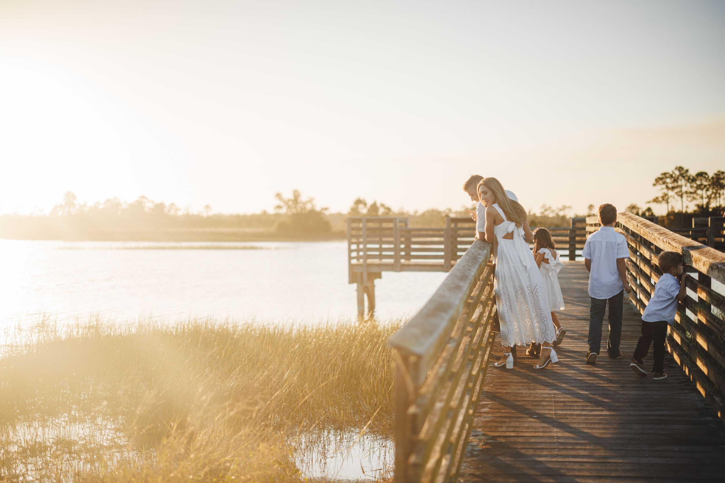 A wooden pier extends over a tranquil lake at sunset with soft golden light illuminating the misty waterscape.