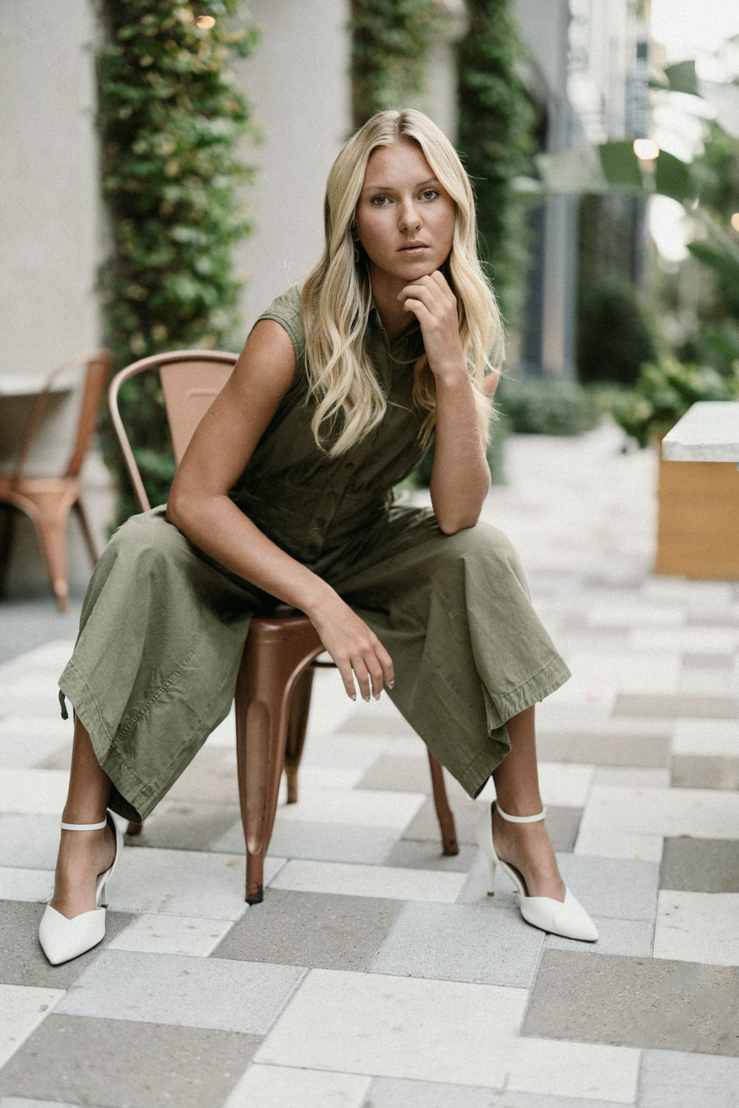 Fashion model poses on concrete steps wearing olive green pants and white mules in modern urban setting.