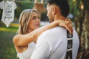 An intimate couple poses together outdoors in casual white attire.