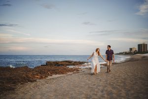 People walking on a scenic coastal path during sunset with ocean views and rocky terrain in the background.