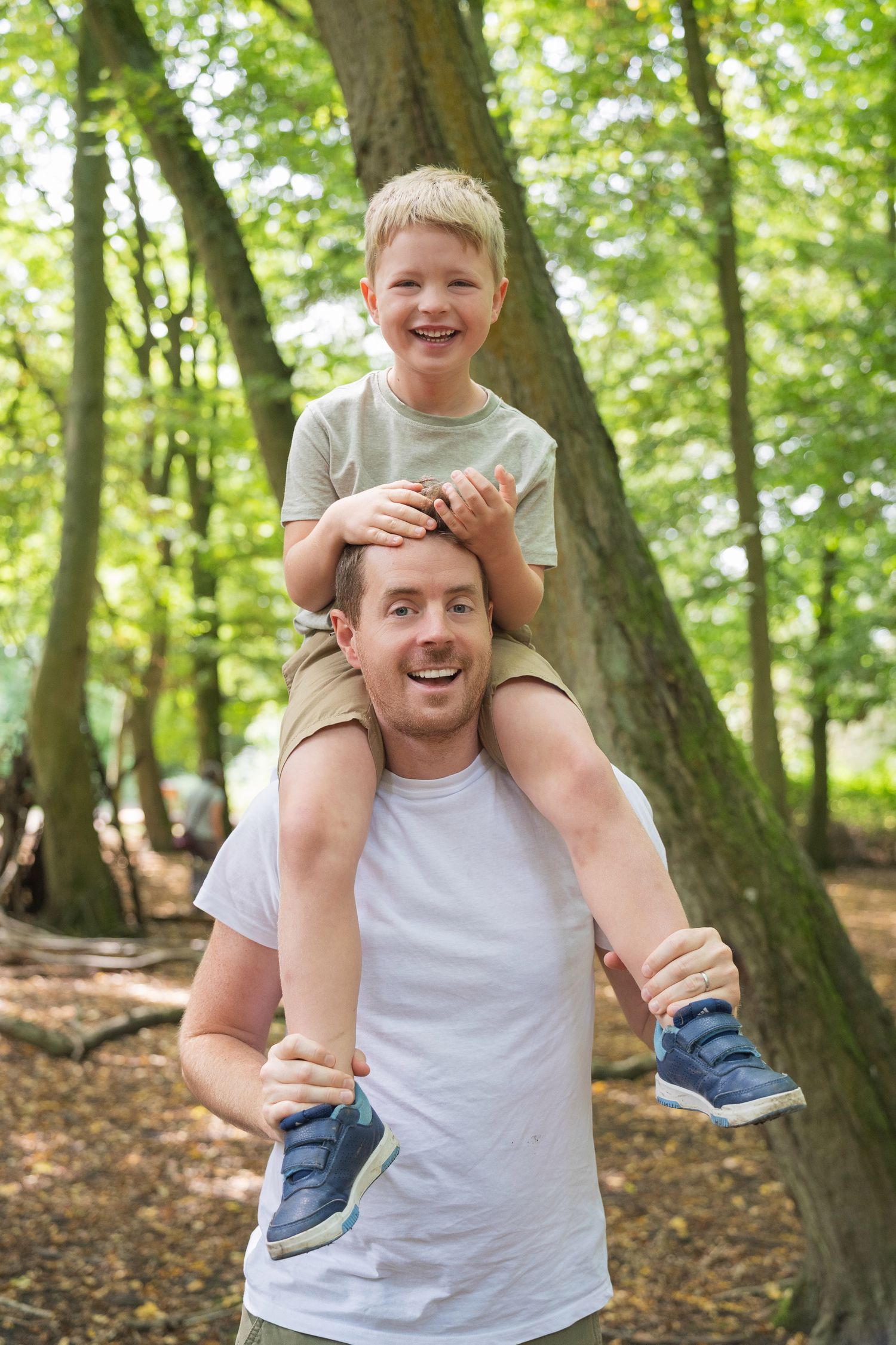 Two children share a joyful moment while sitting together on a fallen log in a sunlit forest.