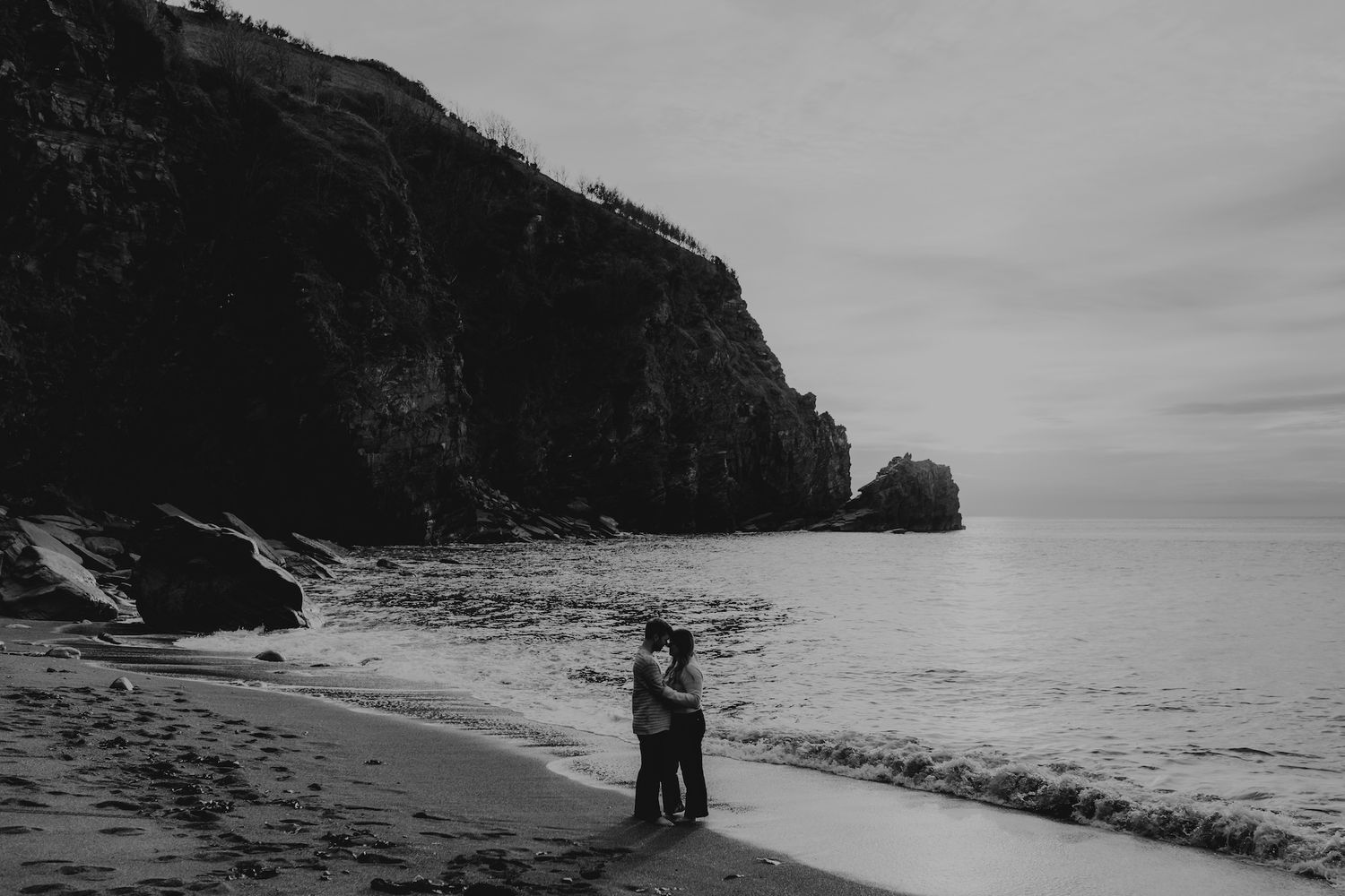Silhouettes of people walking along a dramatic black sand beach with steep cliffs and ocean views.