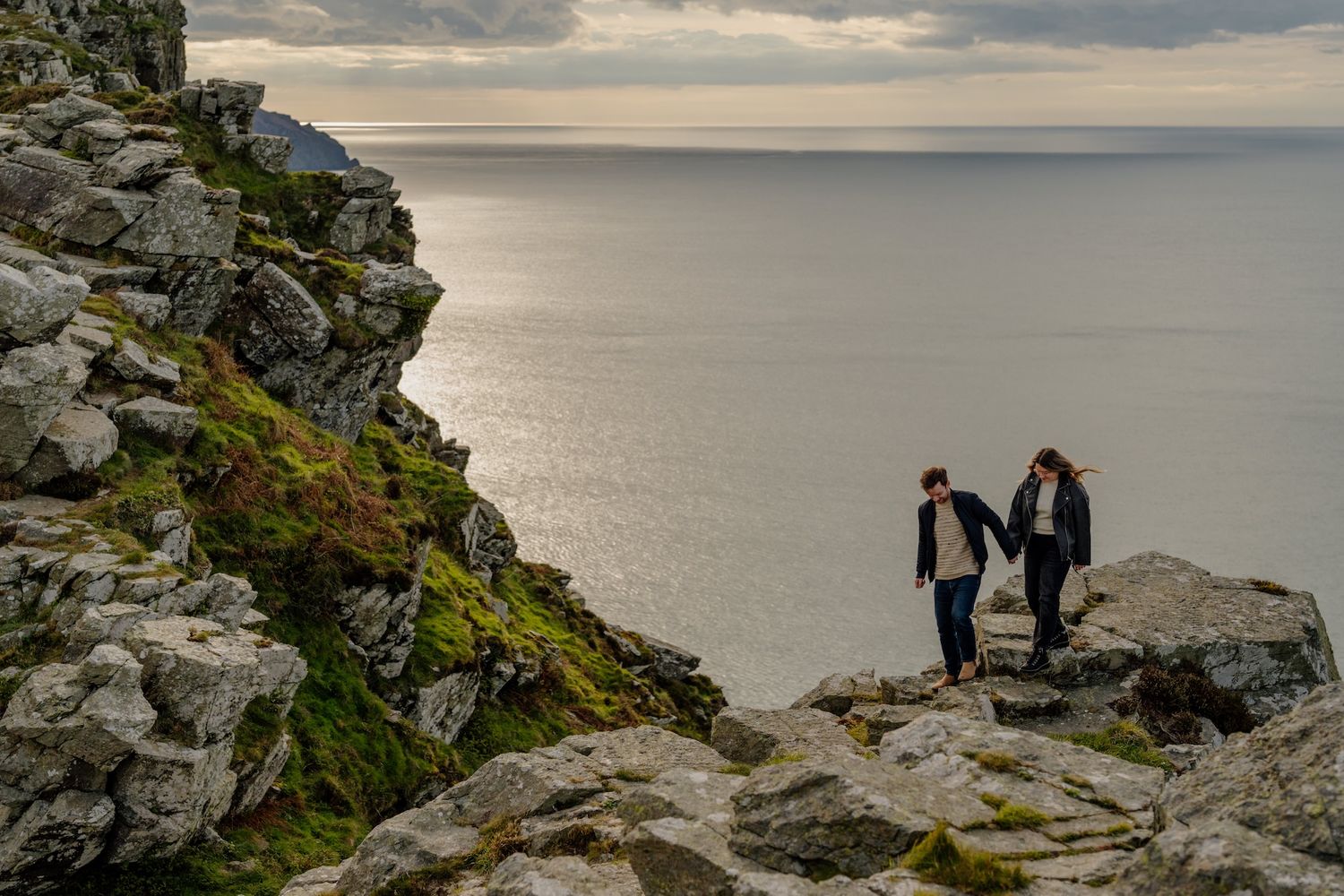 Couple sharing an intimate moment together on a rocky coastal cliff overlooking the ocean at sunset.