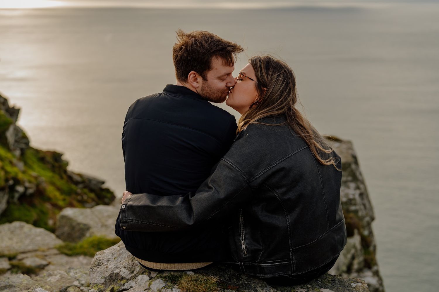 Romantic couple sharing intimate moments on a scenic coastal cliff overlooking the ocean.