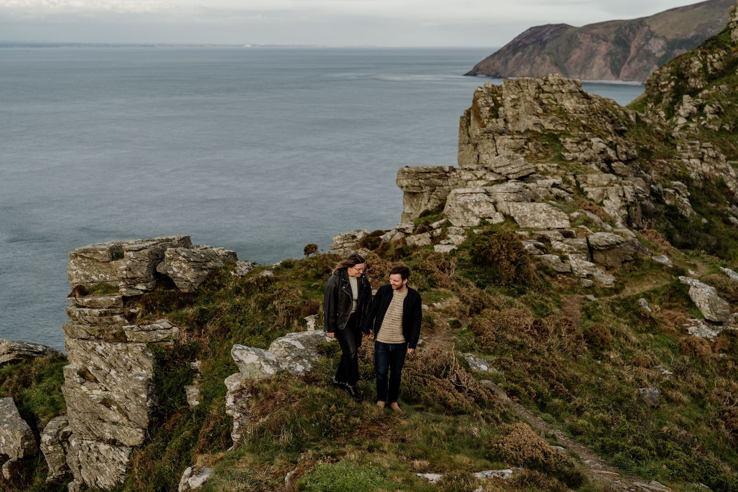 Coastal landscape with rugged cliffs and ocean waves against a moody sky.
