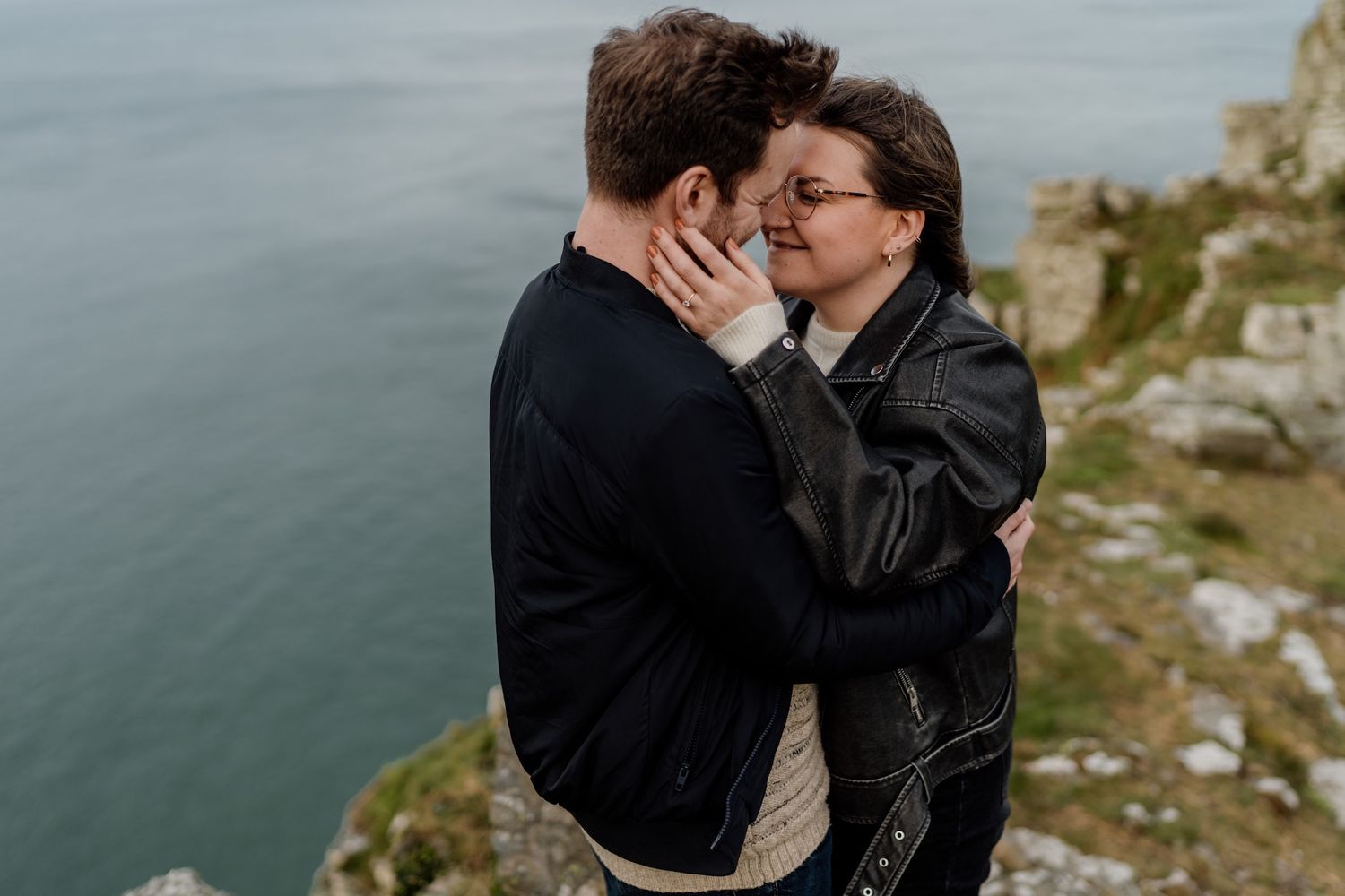 Couple embracing against dramatic seaside cliffs during an outdoor photoshoot.