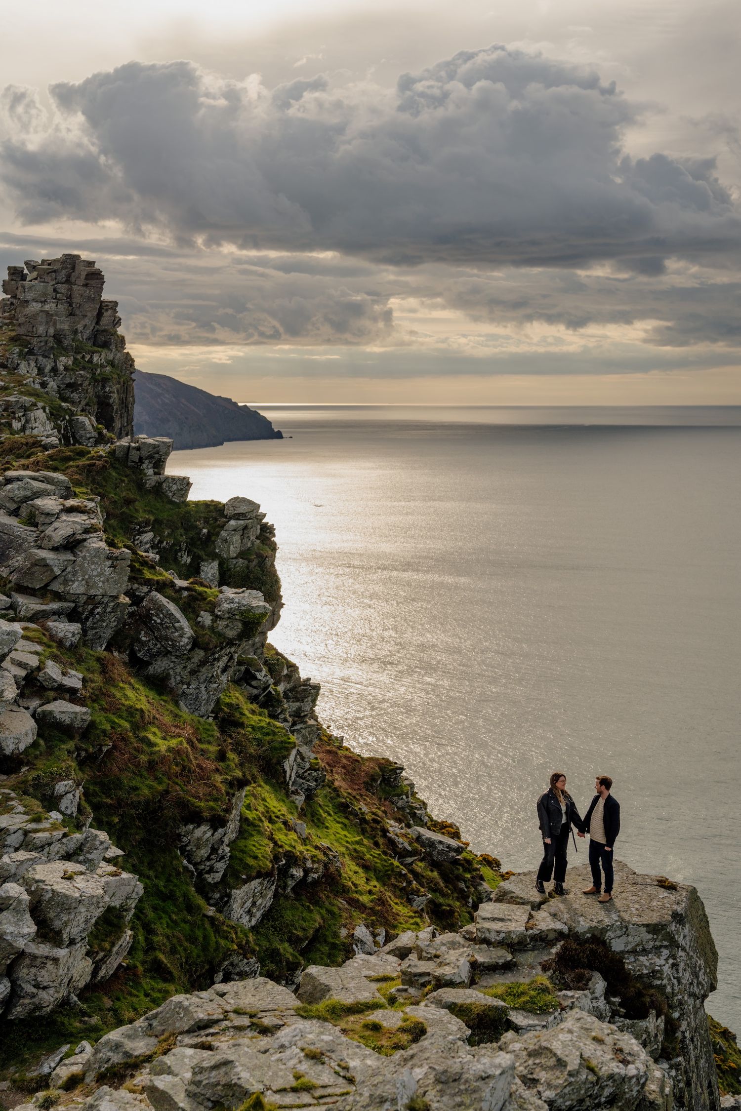 Silhouetted figures stand together on rugged coastal cliffs with a sweeping ocean view.