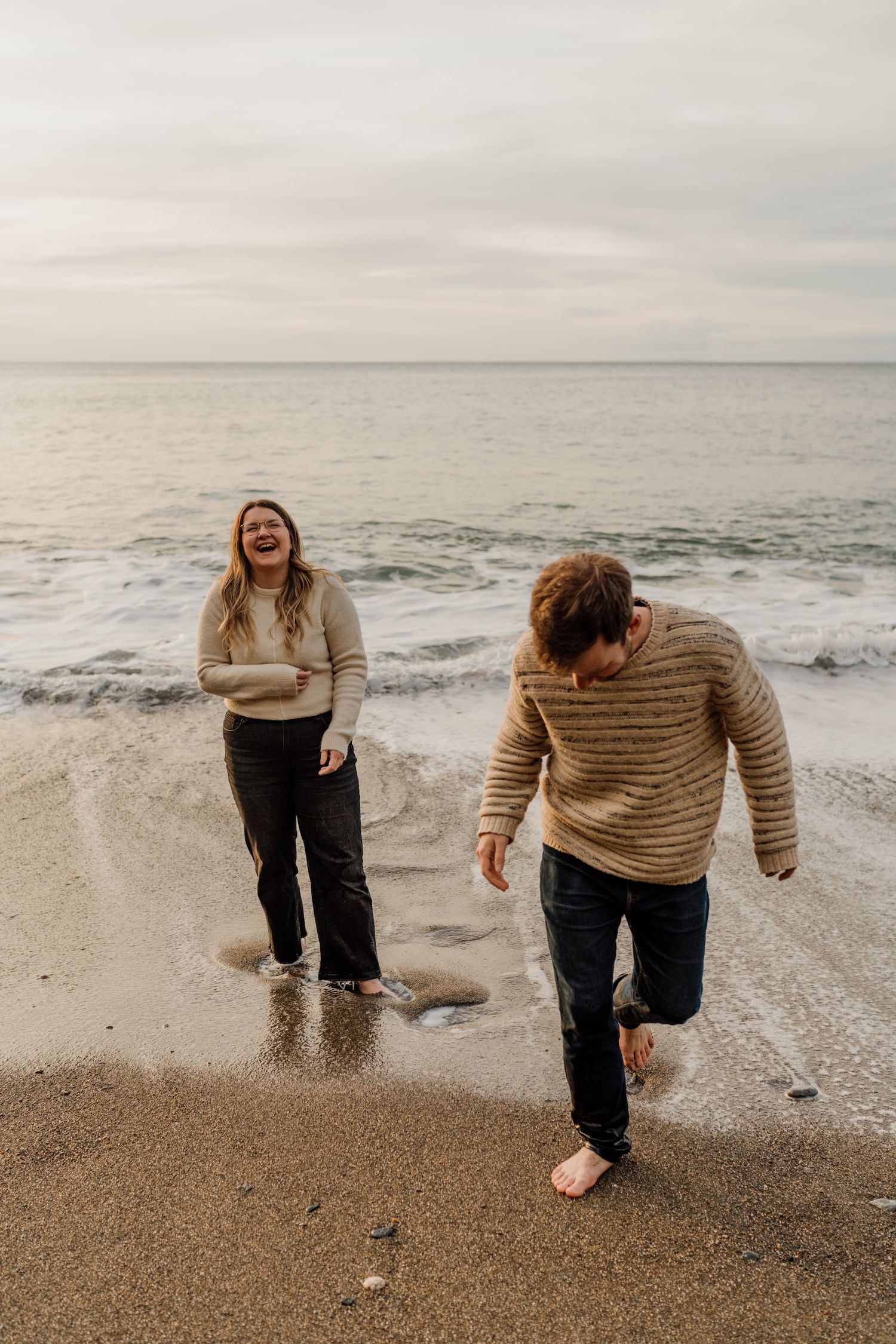 A candid sequence of someone playing and laughing at the beach during a moody overcast day.