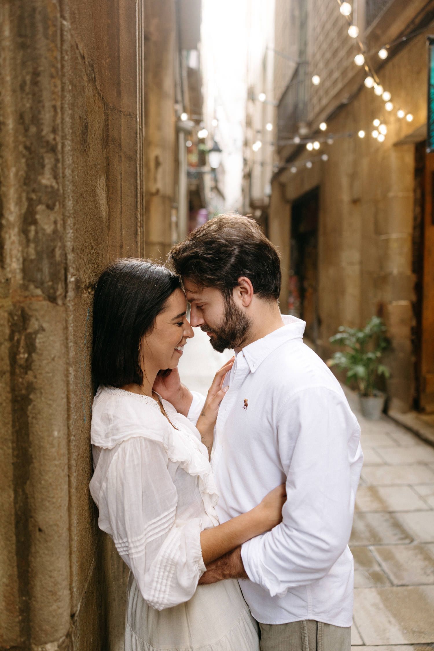 A couple embraces tenderly in a sunlit stone alleyway in Barcelona's Gothic Quarter.