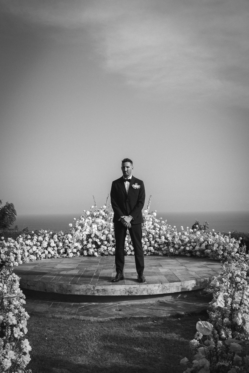 A black and white sequence showing a person sitting on a circular stone platform surrounded by white flowers.