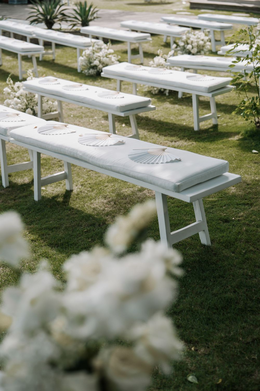 White wooden benches arranged in rows outdoors for a wedding ceremony on a grassy lawn.