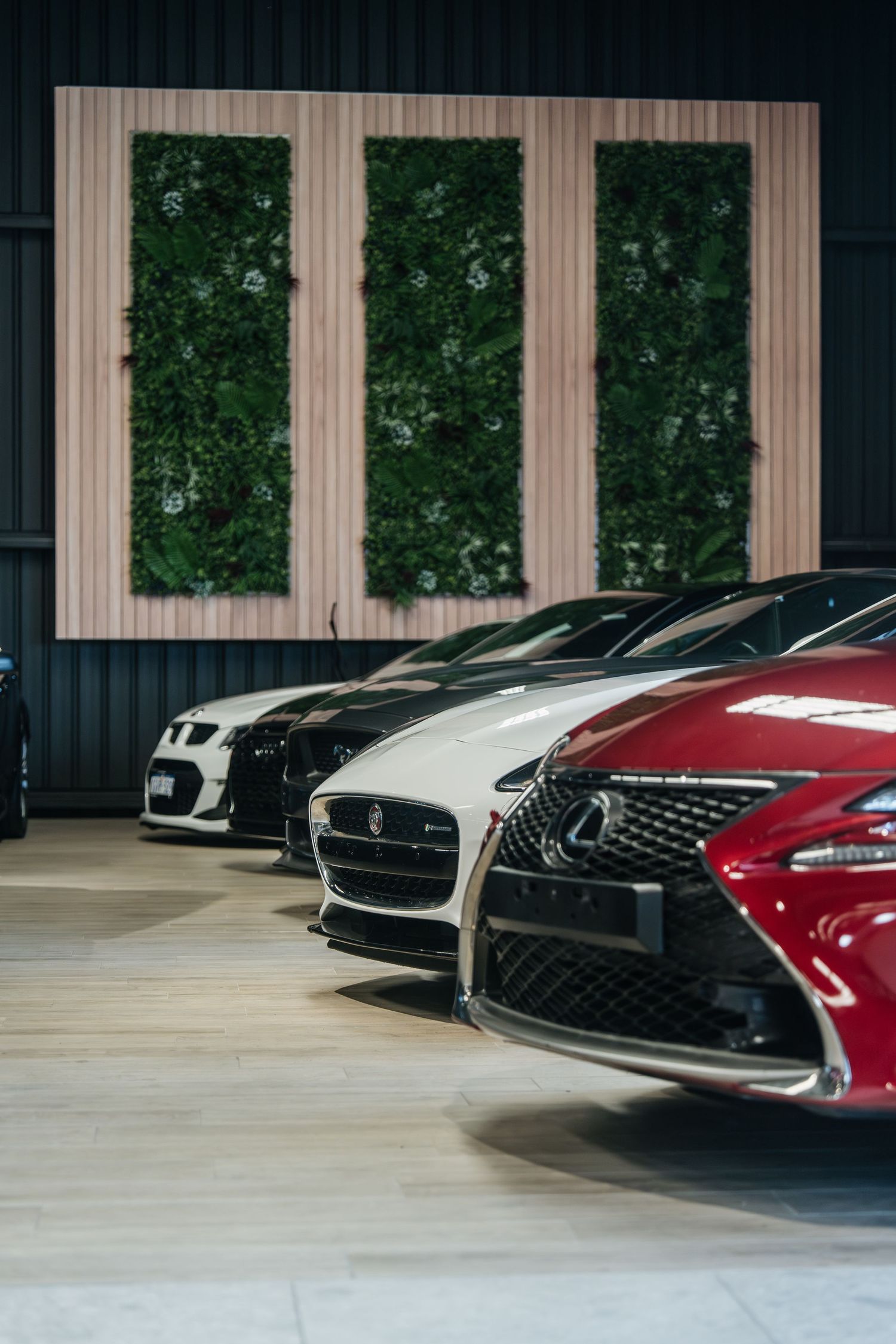 A lineup of luxury cars including Lexus and Infiniti models showcased in a modern showroom with vertical wood paneling.