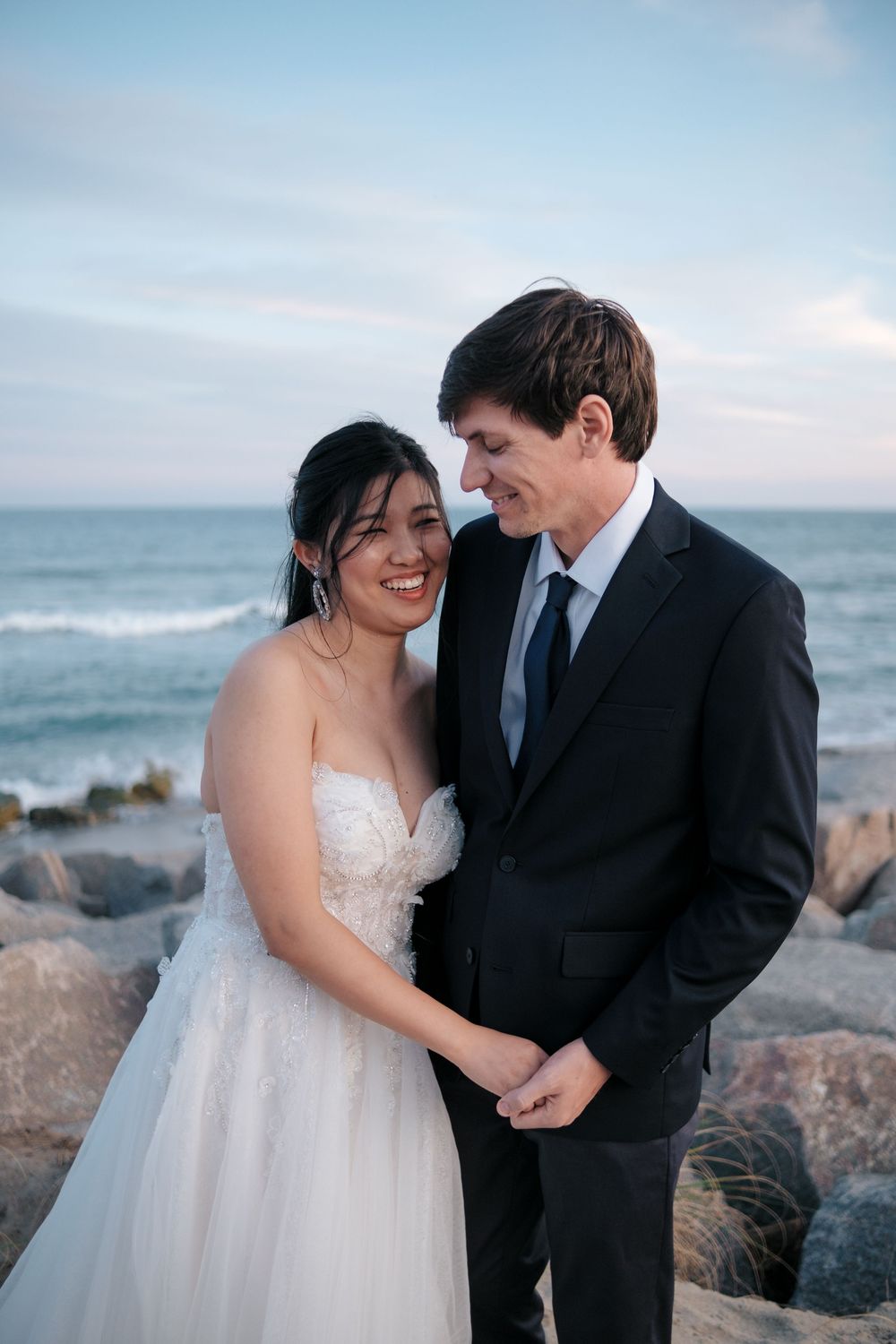 Intimate wedding portraits against a coastal backdrop with rocky shore and ocean waves.