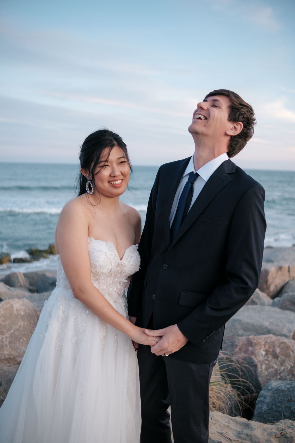 A joyful moment shared between a couple in formal wedding attire by the seaside.